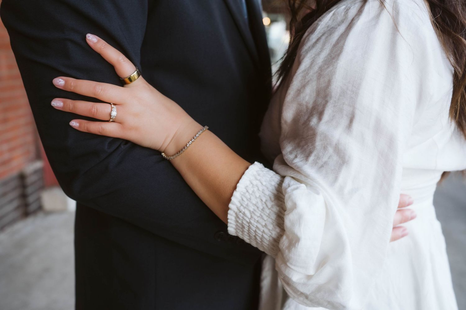 Close-up view of hands embracing with a white sleeve and black jacket sleeve visible.