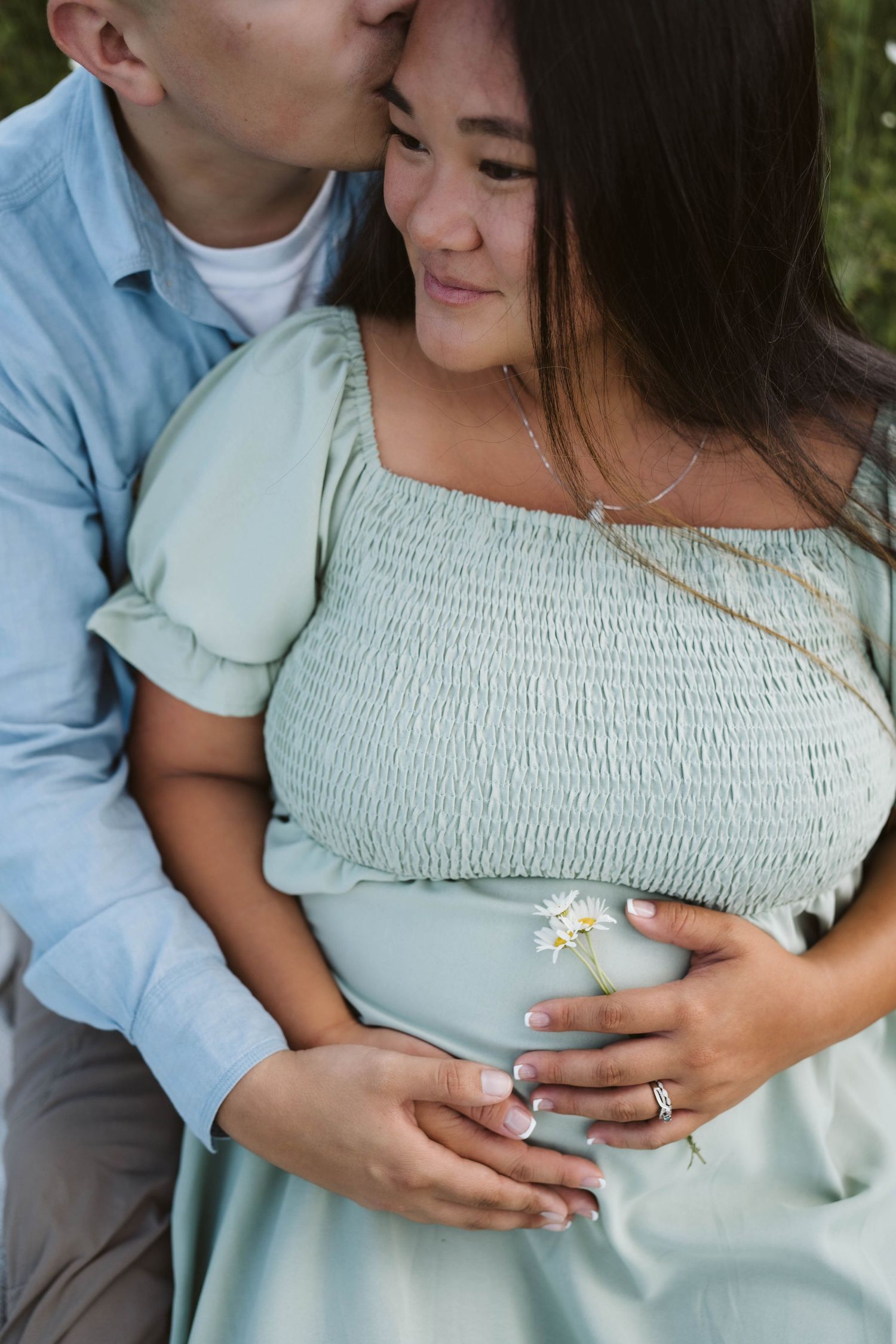 A tender romantic moment captured outdoors with a mint green smocked dress and delicate wildflower.
