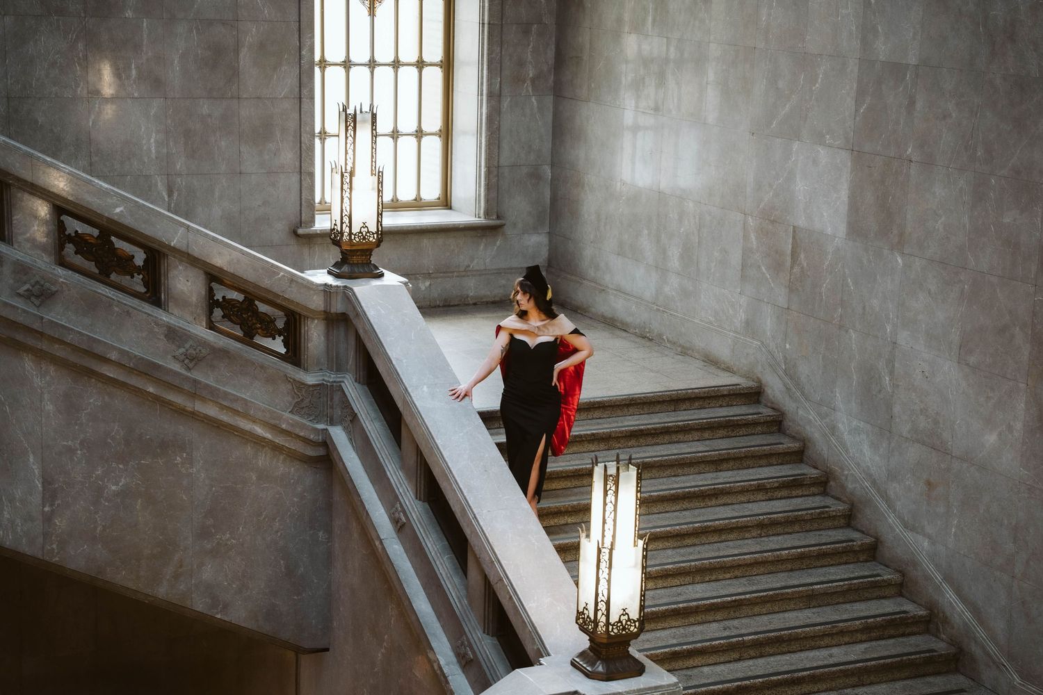 A couple embraces on a grand stone staircase with ornate architectural details and natural lighting from above.