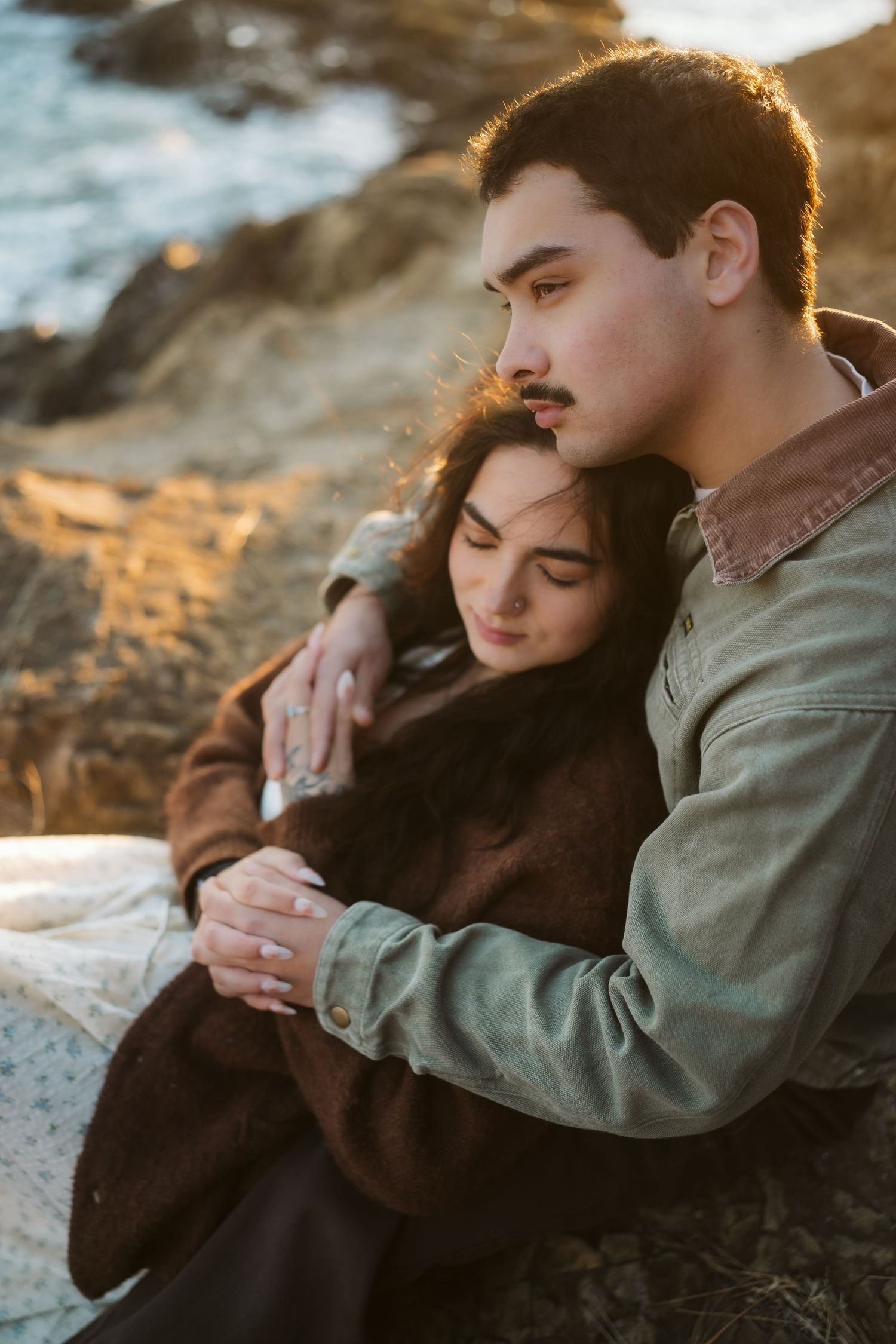 Intimate couple embracing on rocky coastal cliffs during golden hour.