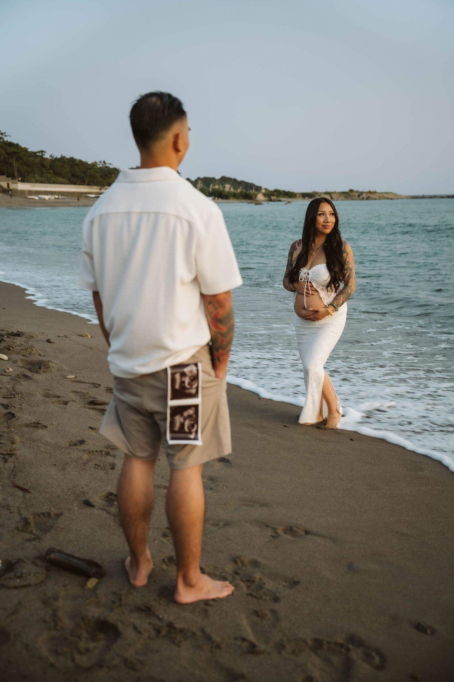Two people stroll along a dark sandy beach with ocean waves in the background.
