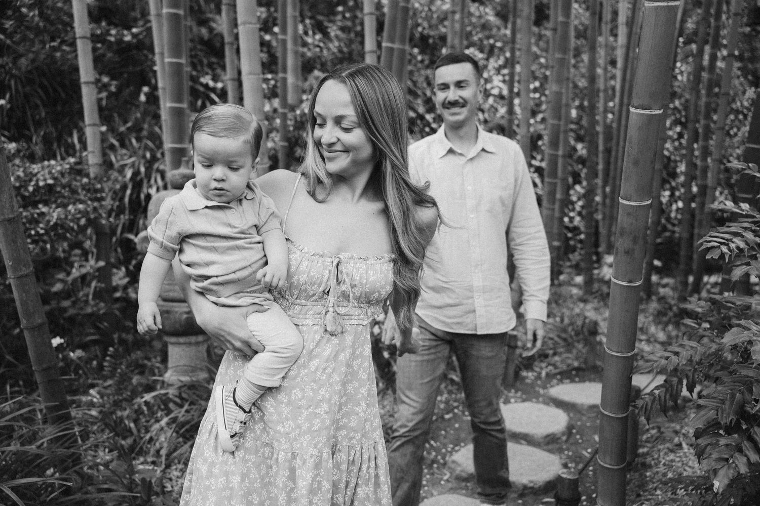 A collection of black and white family portraits taken outdoors in a wooded setting shows tender moments between loved ones.