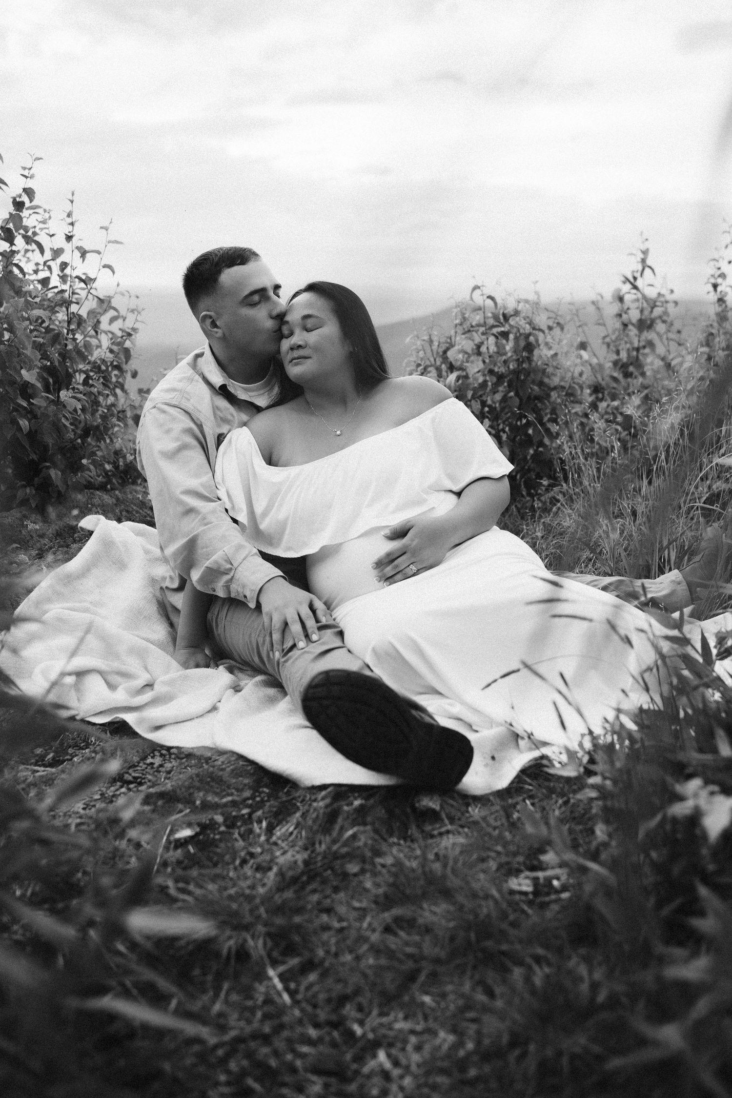 A romantic black and white portrait of a couple embracing on a blanket in a wildflower meadow.