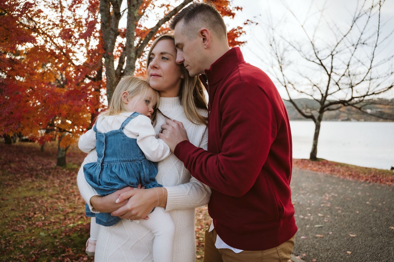 A couple embraces outdoors during autumn with vibrant red and orange fall foliage in the background.