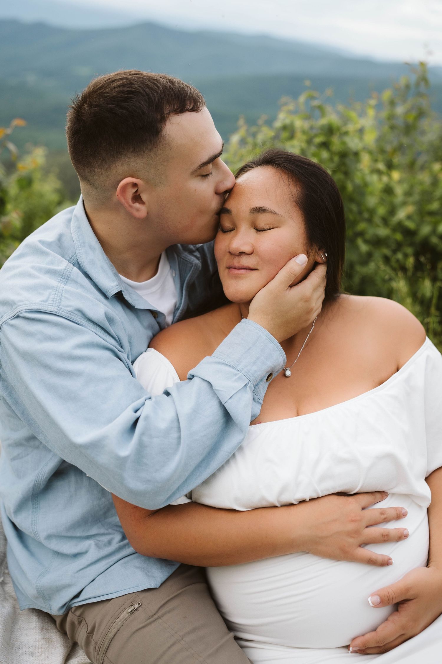 A couple shares an intimate moment outdoors in nature as they embrace for a maternity photo.