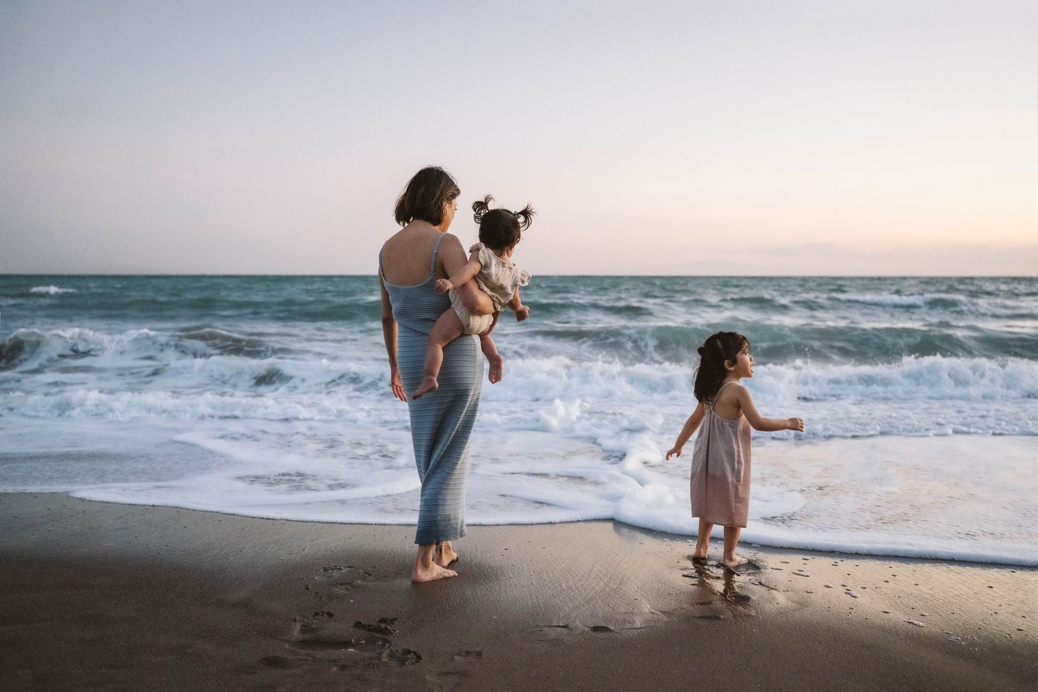 People walking along the shoreline at dusk as gentle waves roll onto the beach.