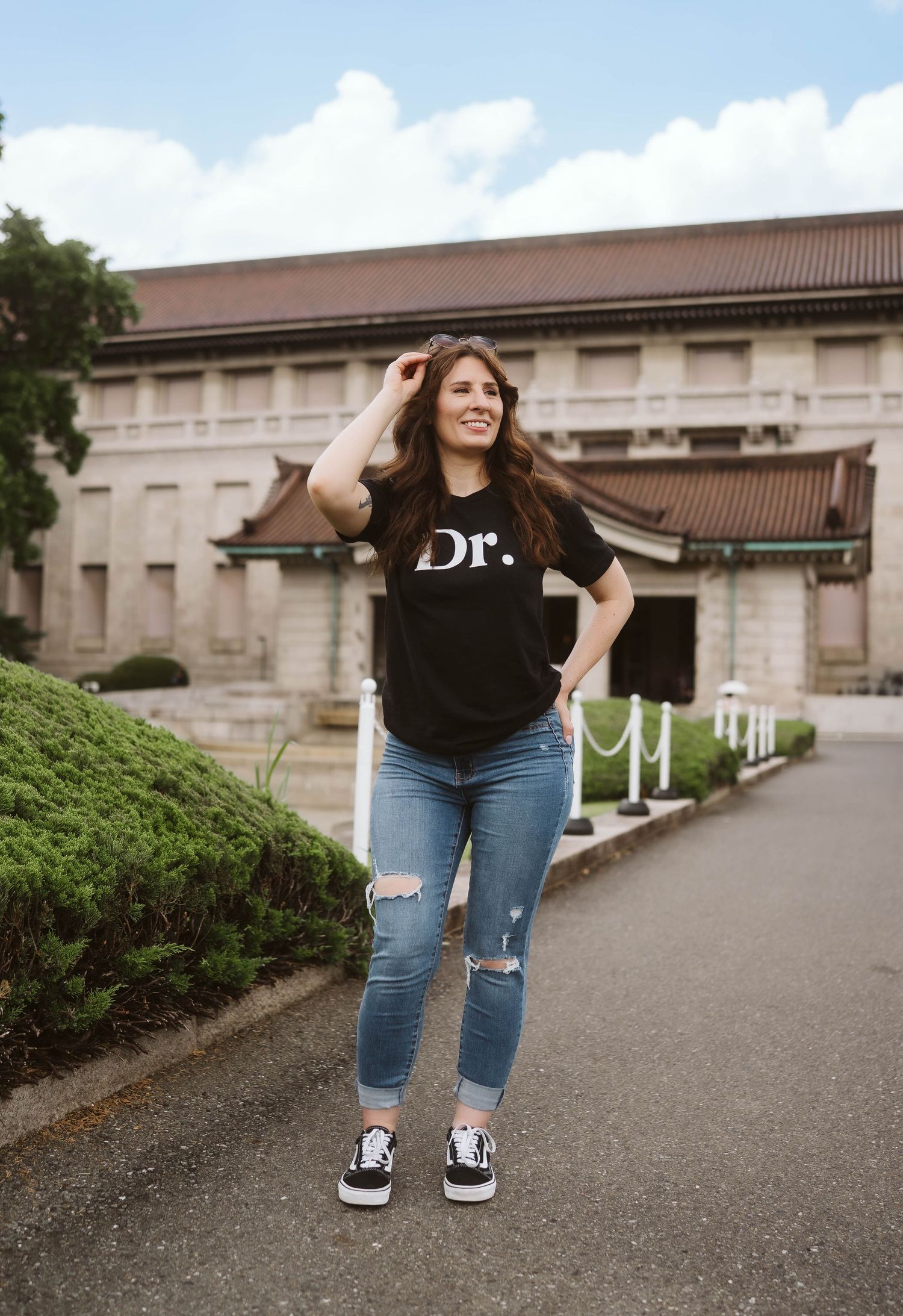 Casual outdoor portrait showing ripped jeans and sneakers against institutional building backdrop.