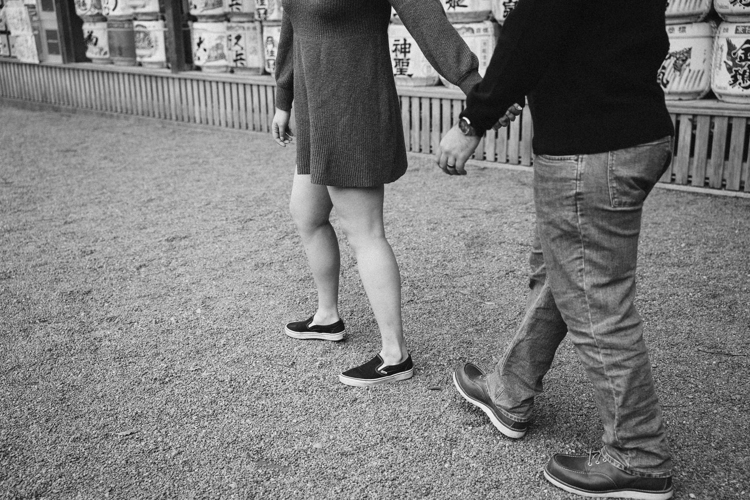 Black and white photo showing legs and feet of two people standing together on gravel ground.