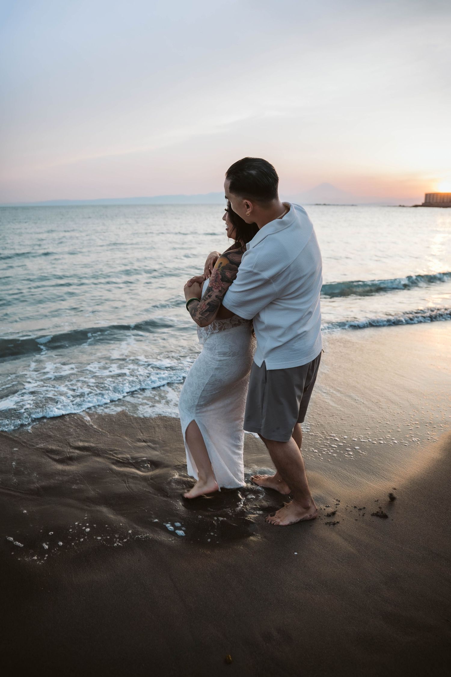 A couple embraces while standing in the surf during sunset at the beach.