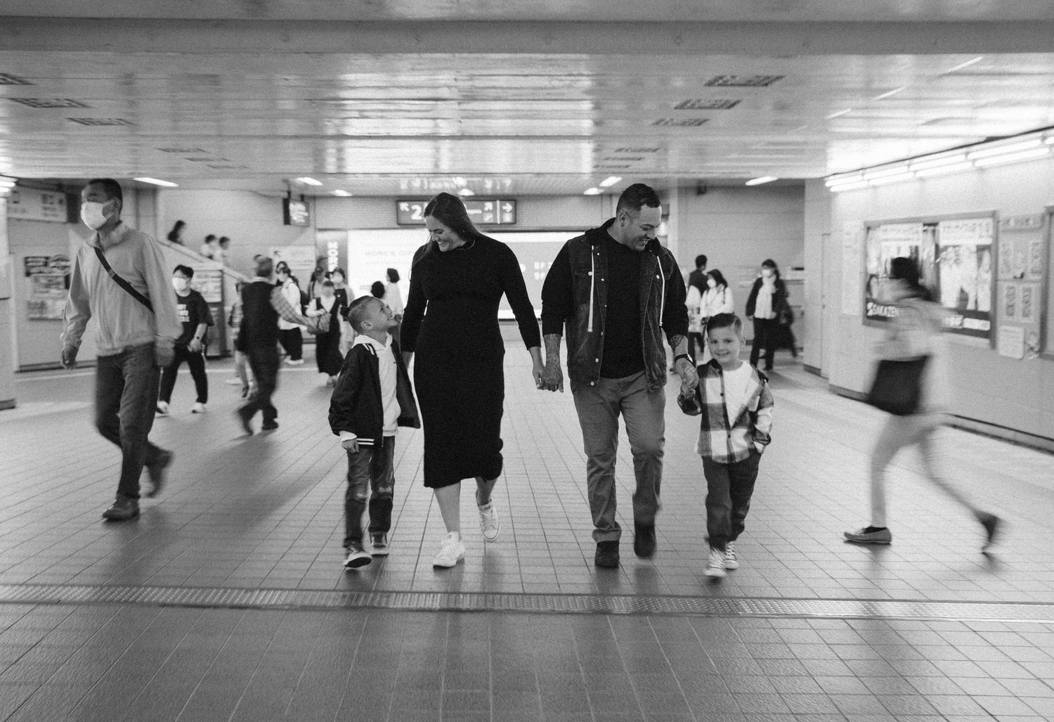 People walking through a modern underground pedestrian tunnel with white tiled walls and bright lighting.