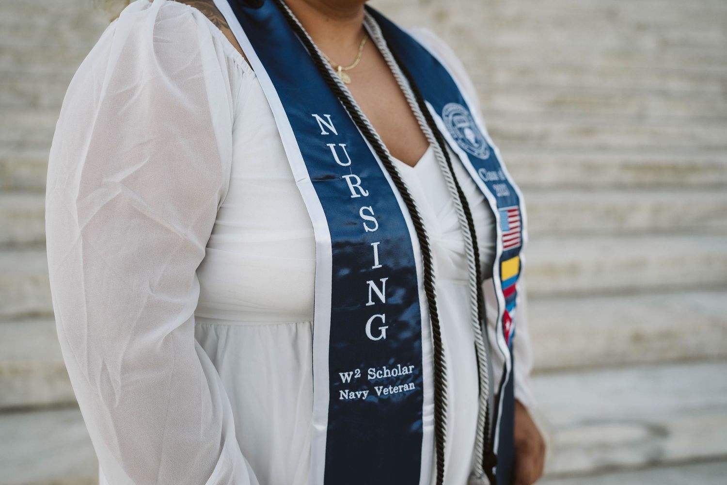 Graduate wearing white jacket with navy blue nursing graduation sash featuring embroidered text and emblems.
