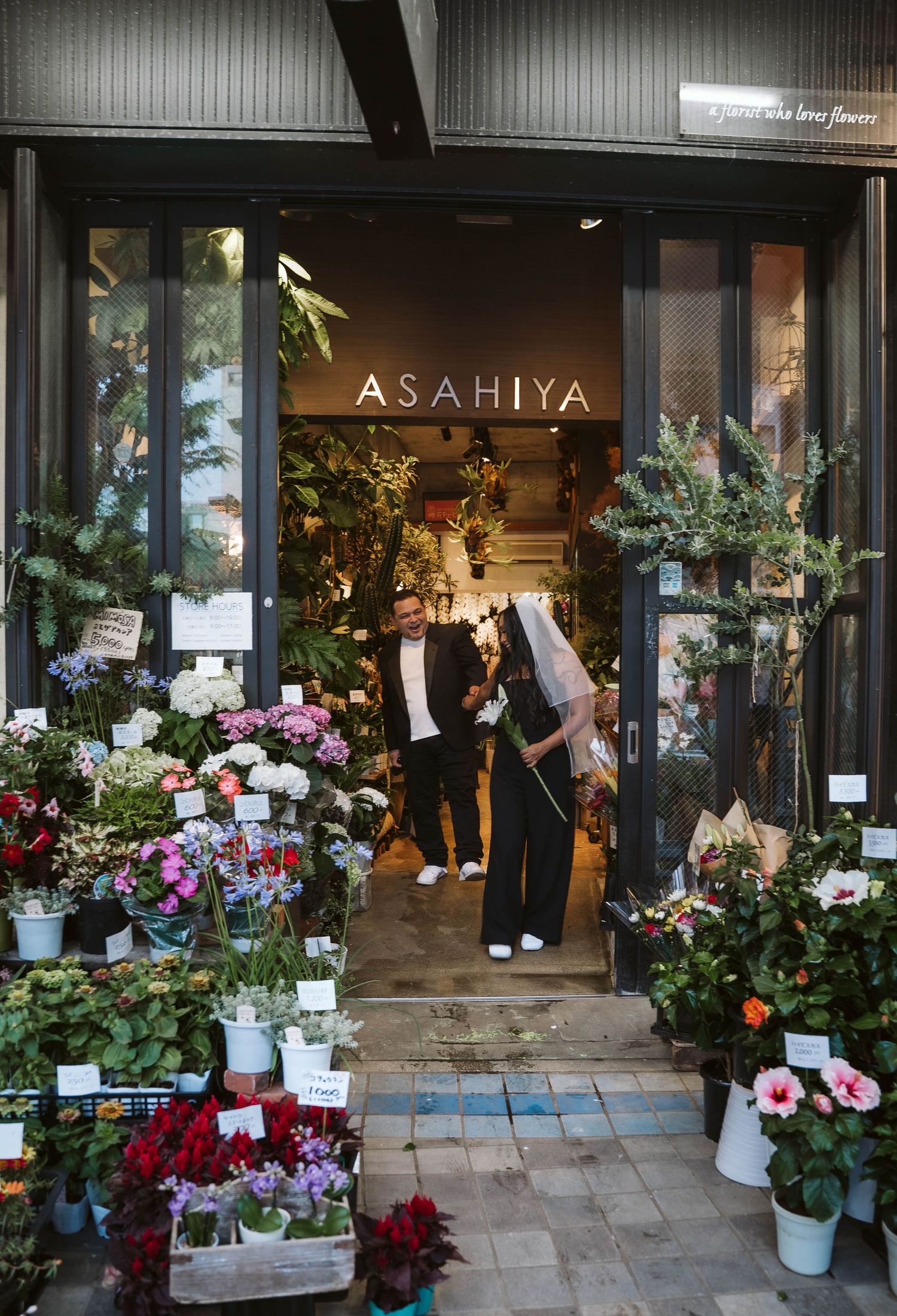 Storefront of Asahiya shop with colorful floral displays and potted plants arranged outside the entrance.
