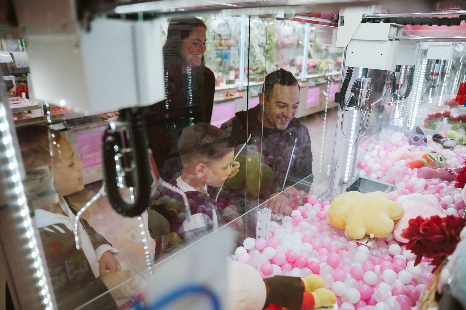 People browse and play arcade games in a colorful Japanese arcade filled with pink claw machines and prizes.
