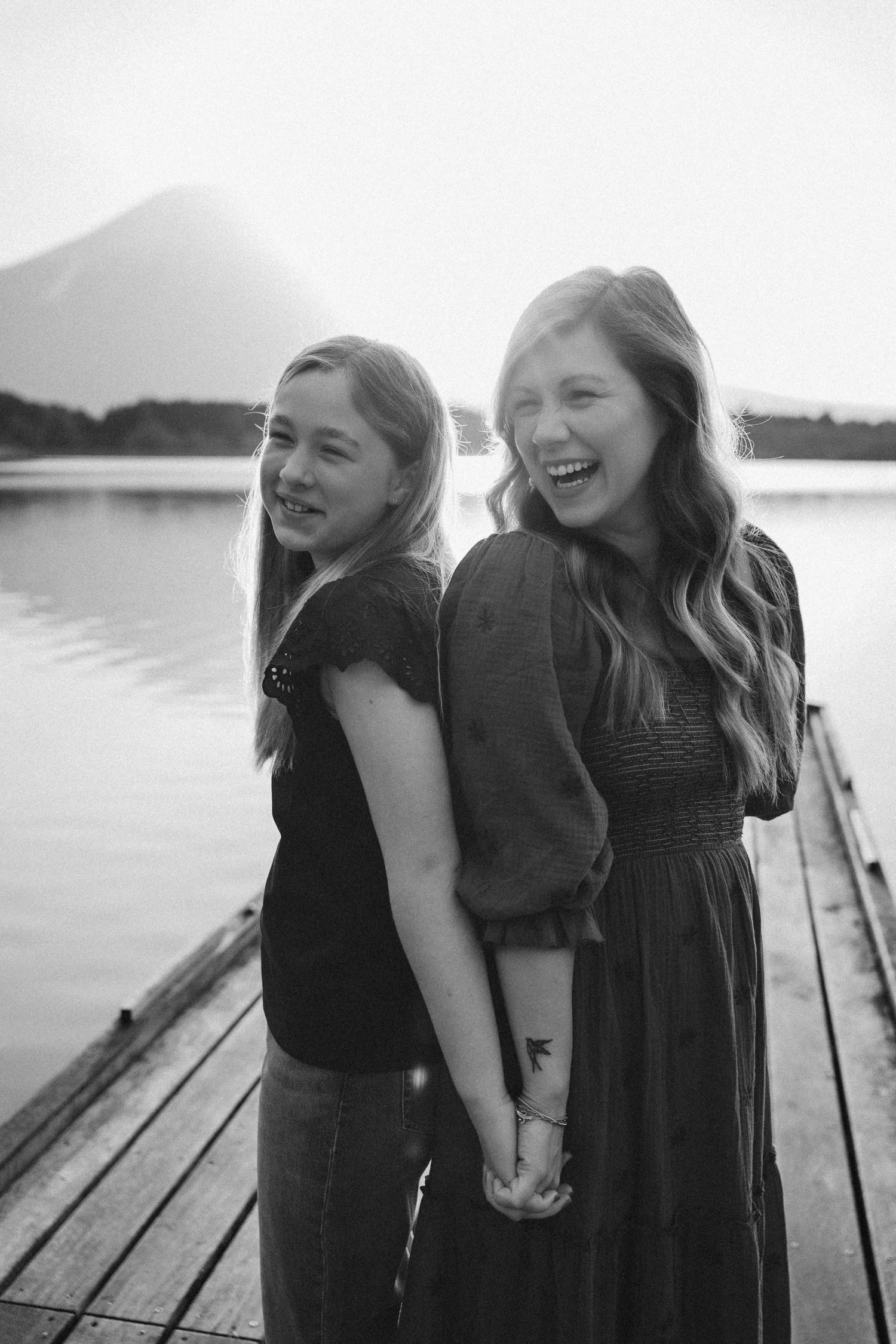 Two people laughing together while holding hands on a wooden dock by a lake in black and white.