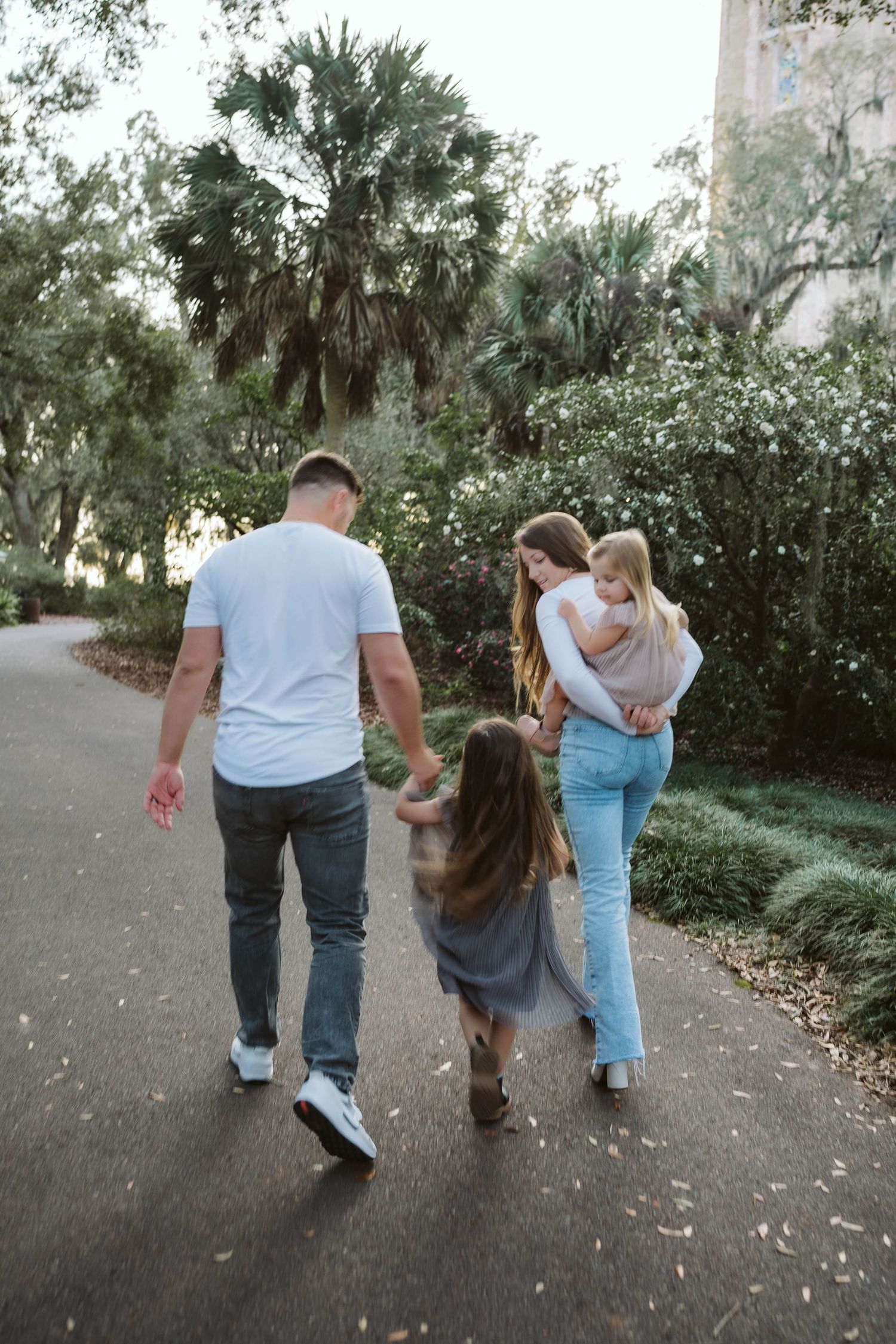 A couple walking down a tree-lined path with children on a sunny afternoon in a park setting.