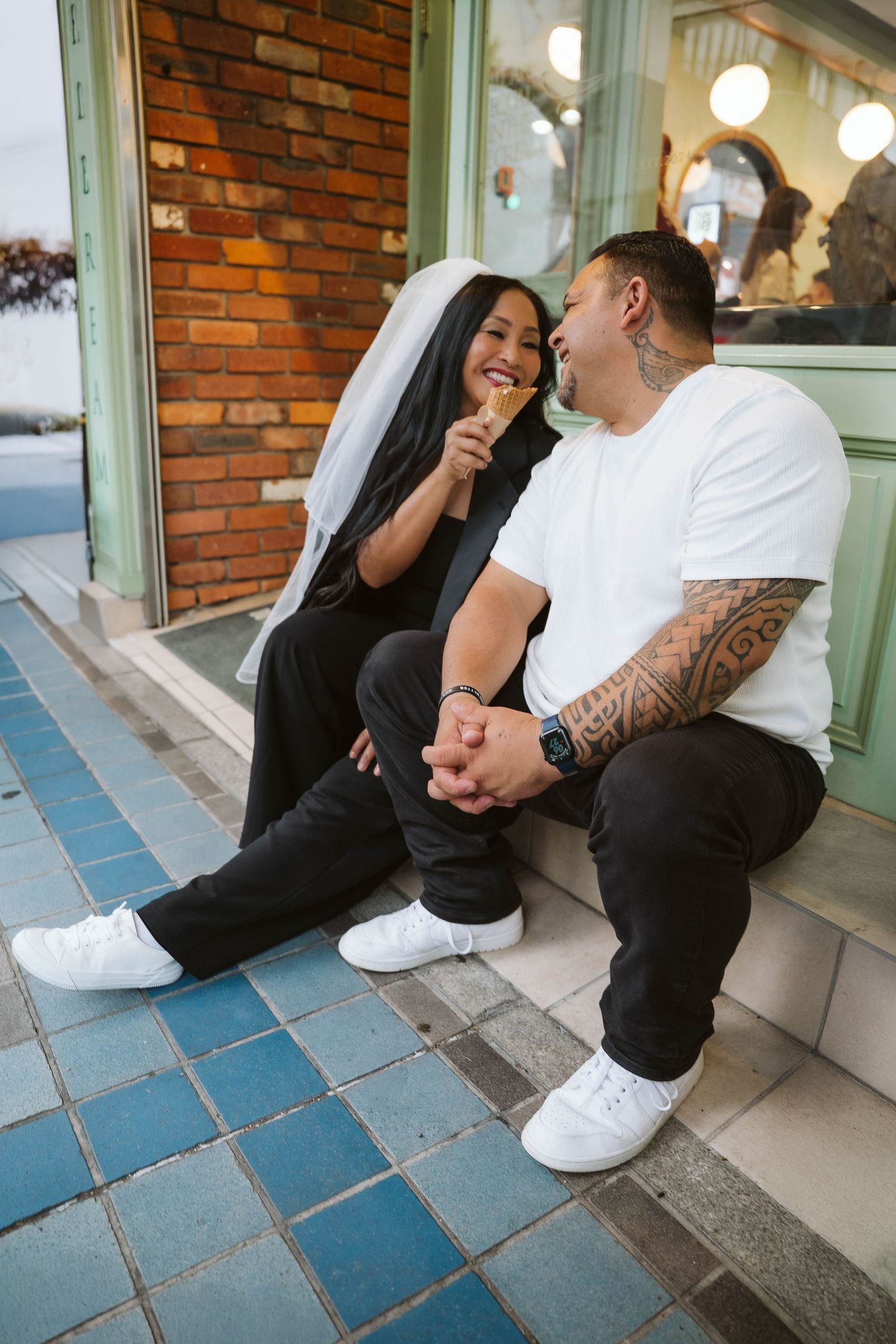 Two people sitting on blue tiled steps outside a brick building, sharing a casual moment together.