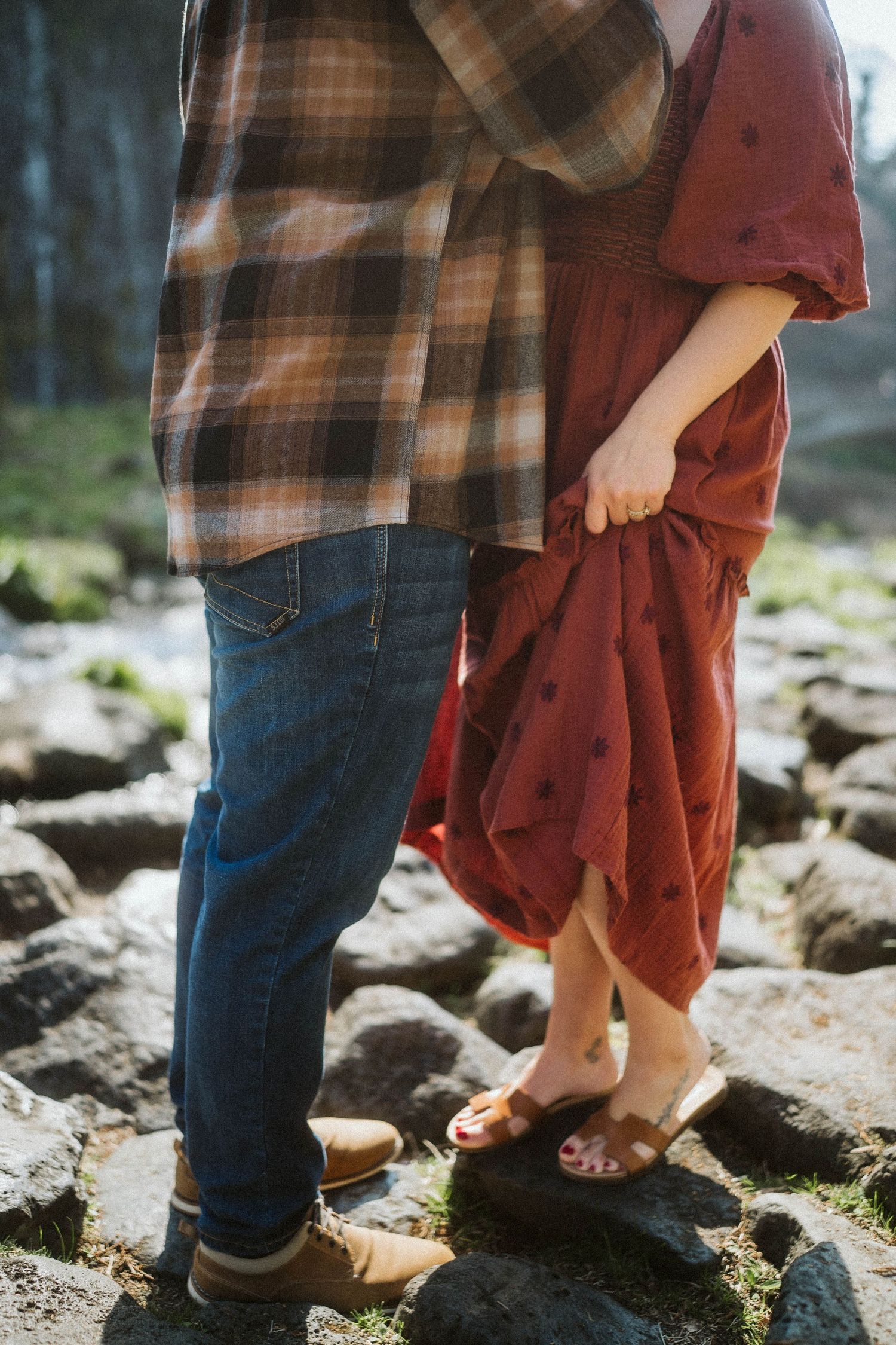 Close-up view of two people's feet standing on mossy rocks wearing plaid and burgundy clothing with denim jeans.