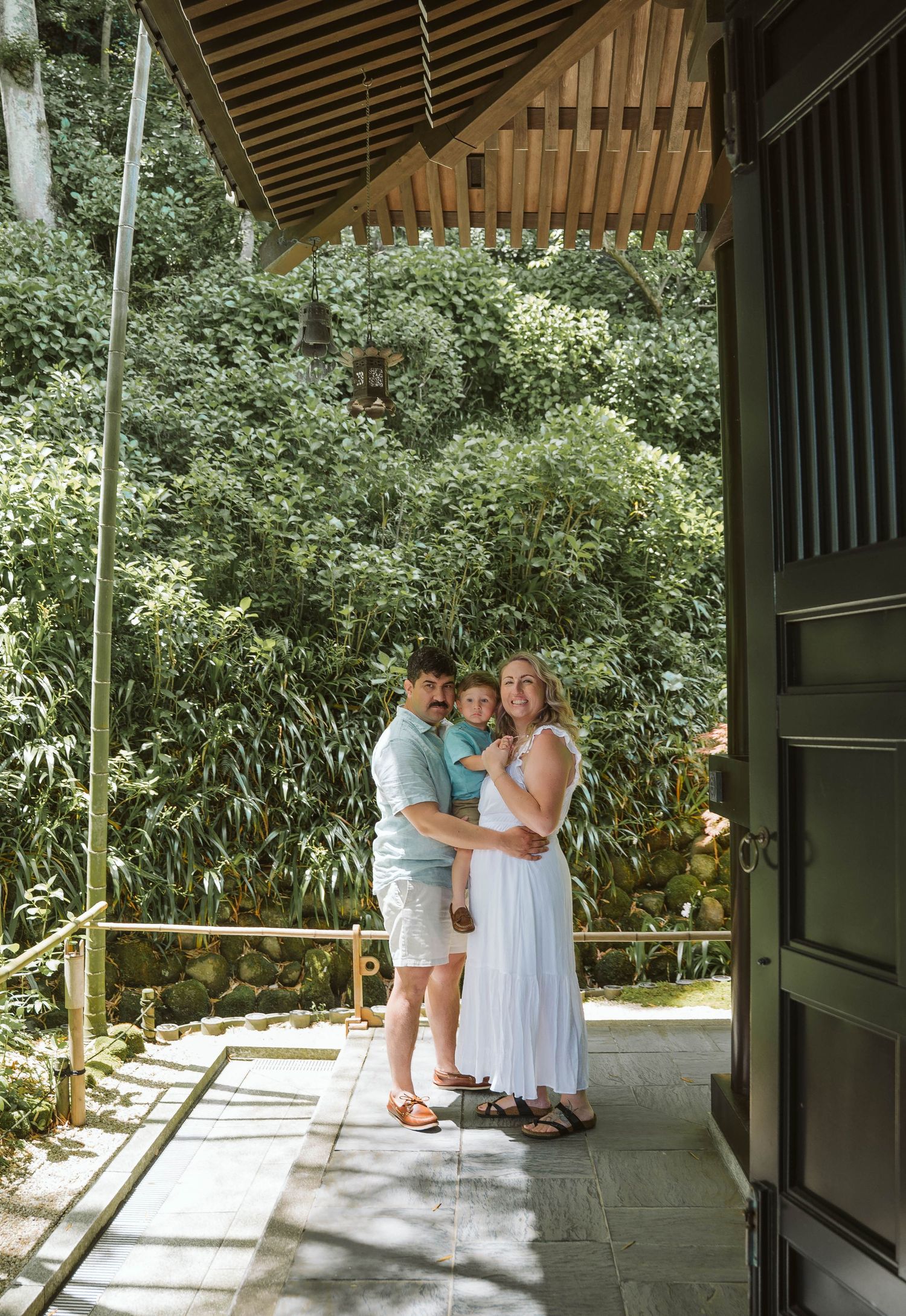 A group gathers on a covered porch with bamboo and greenery visible in the background on a sunny day.