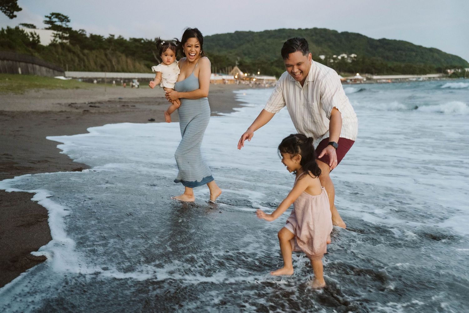 Family enjoying a playful moment together at the beach during sunset as waves crash on the shore.