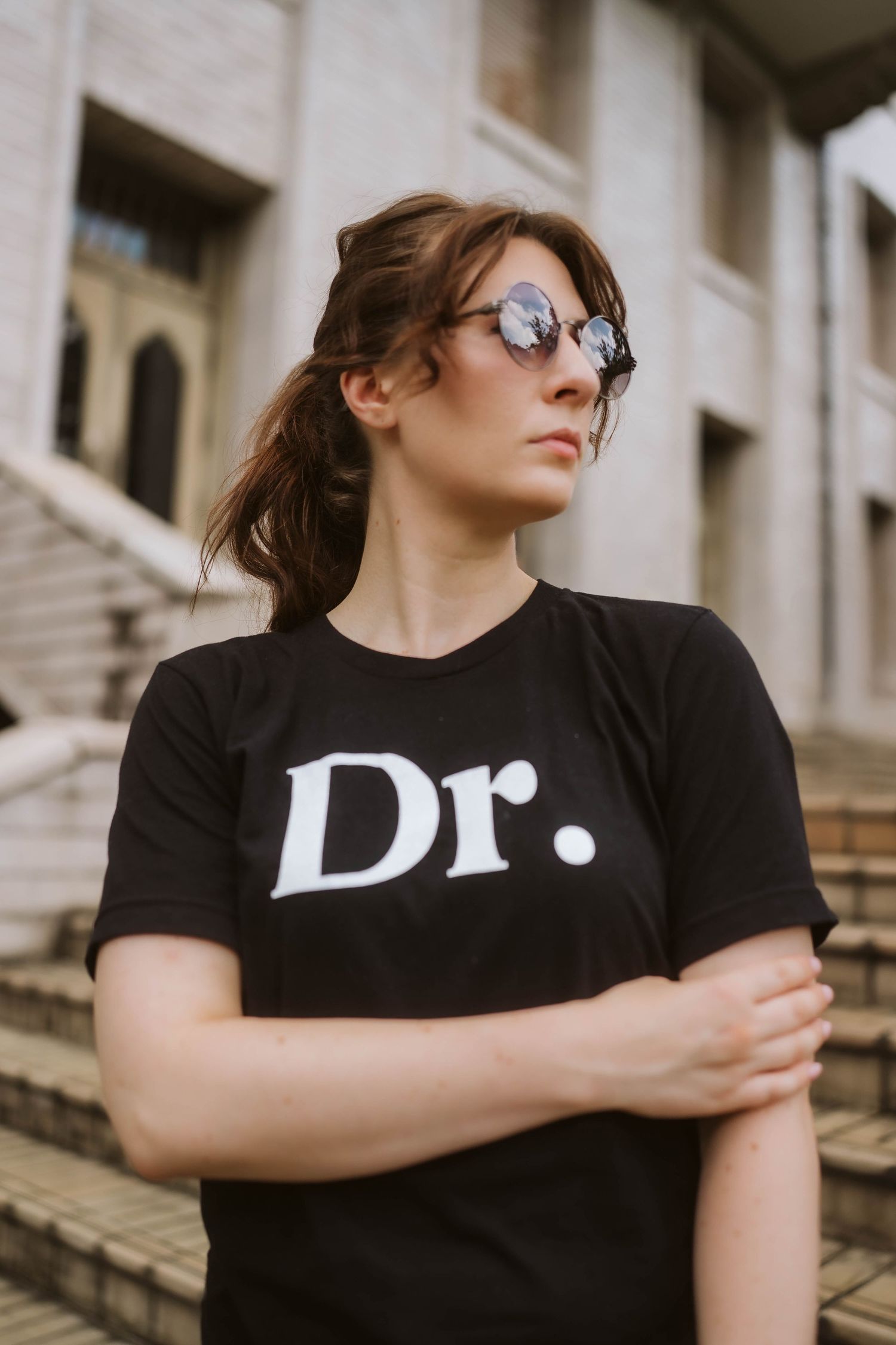 Person in black t-shirt with text sits outdoors with sunglasses in an artistic portrait series.