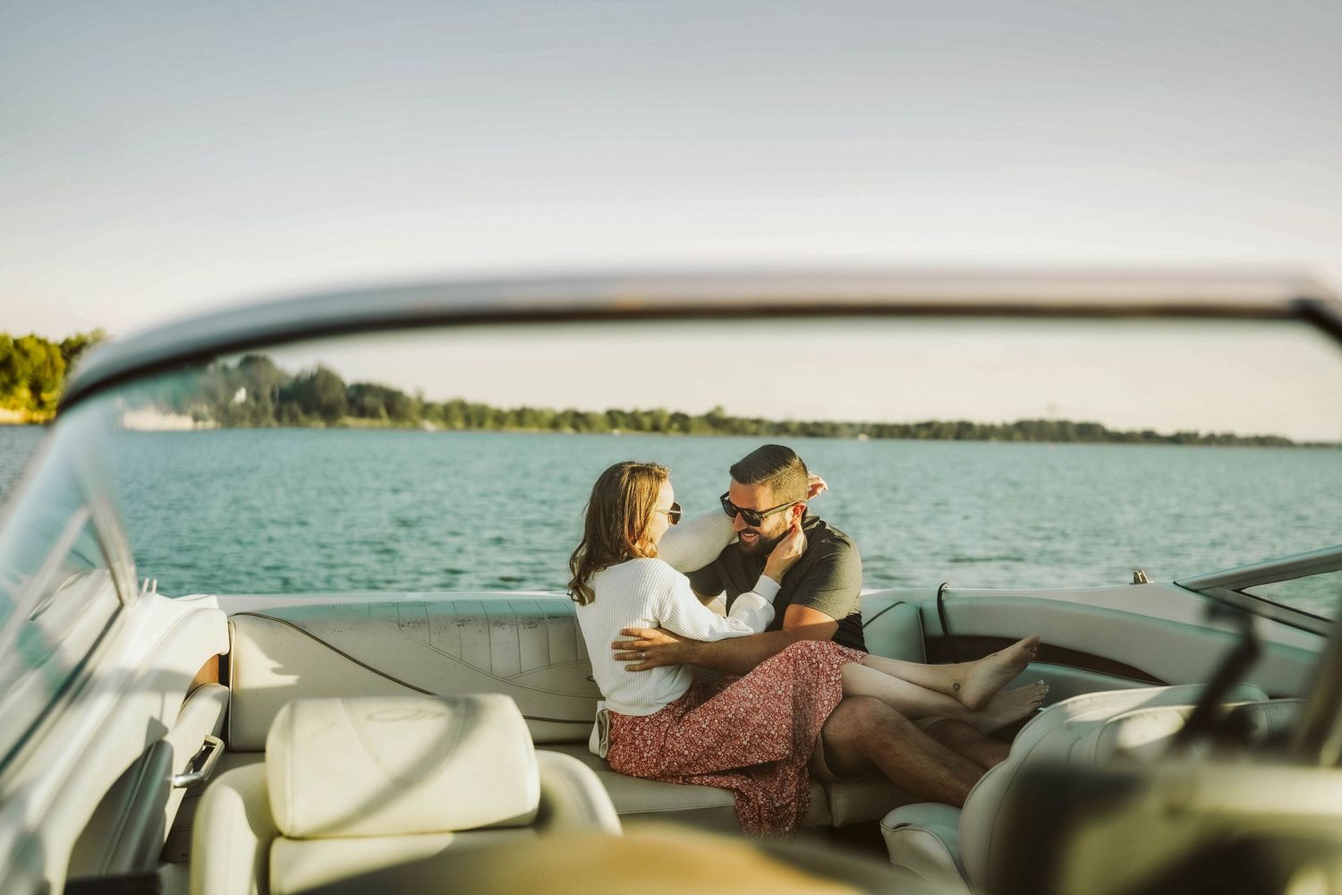 A romantic moment captured in the back seat of a vintage car overlooking a serene lake on a sunny afternoon.