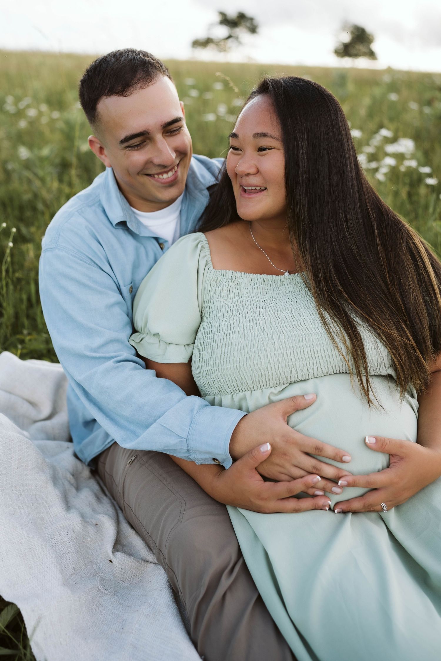 A happy couple embraces while sitting on a blanket in a wildflower meadow during a sunny summer day.