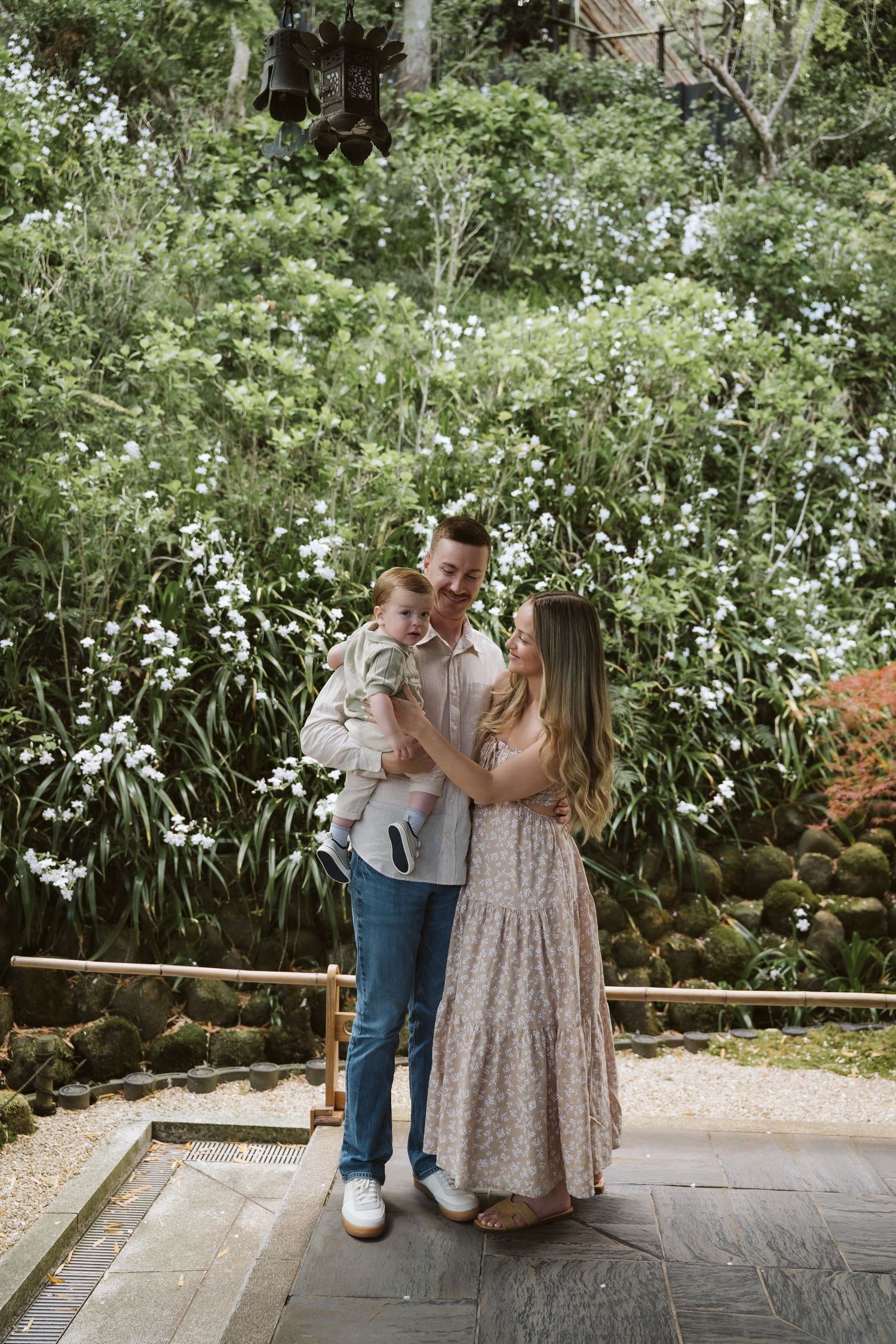 Family sharing tender moments together in front of blooming white flowers at Japanese garden.