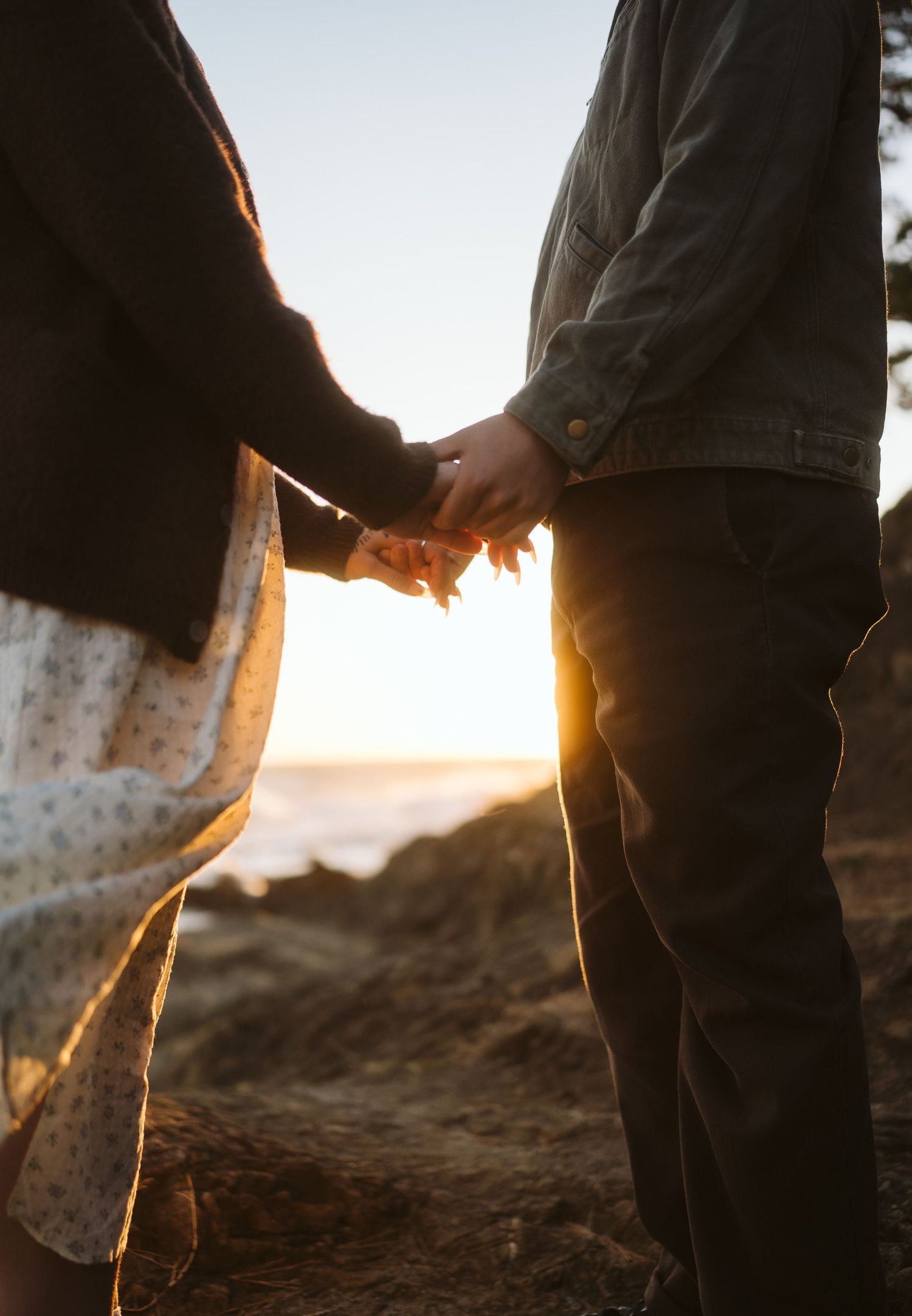 Silhouetted figures standing together against sunset on coastal rocks with ocean waves.
