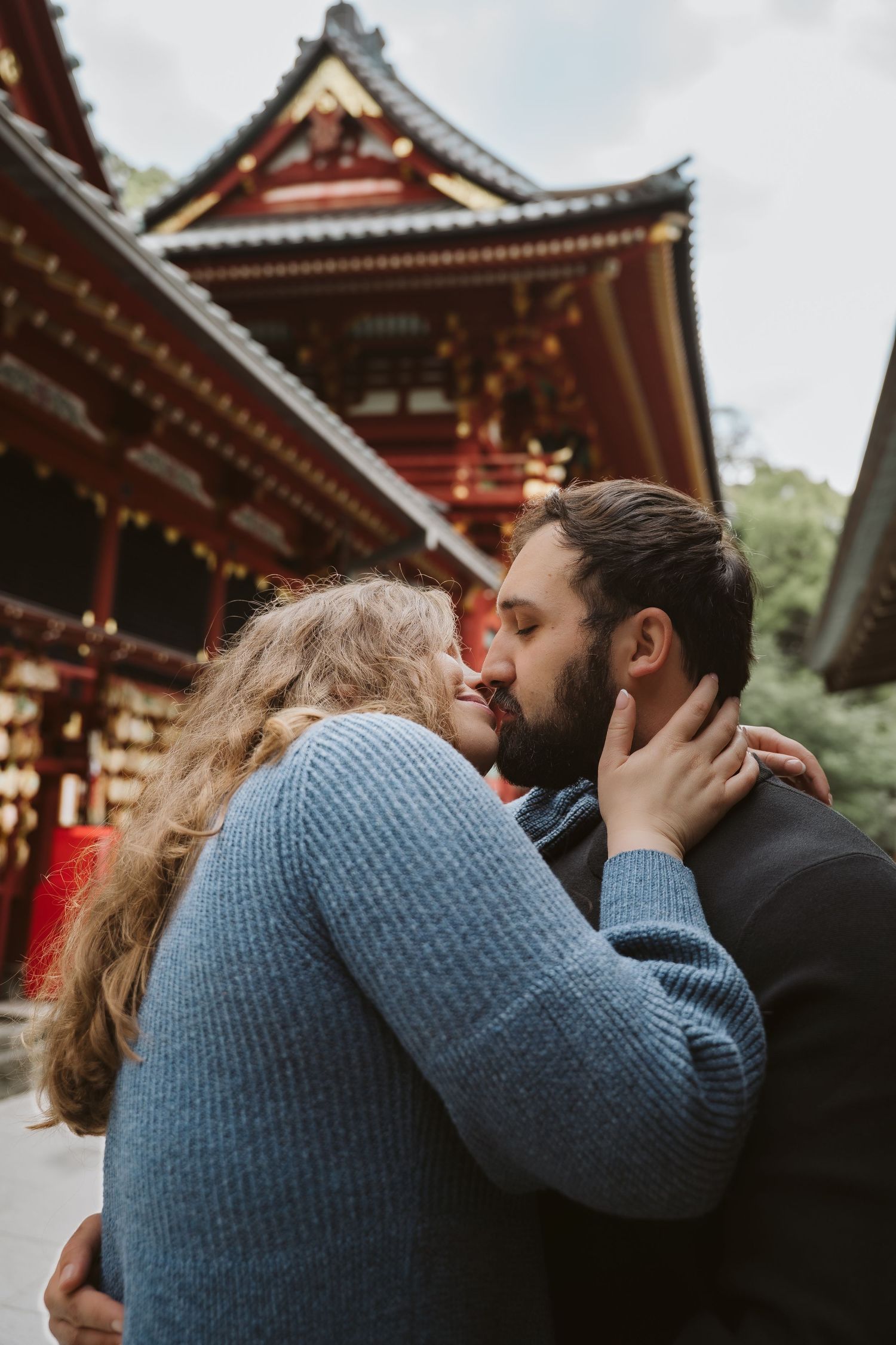Romantic couple sharing intimate kisses in front of traditional Japanese temple architecture.