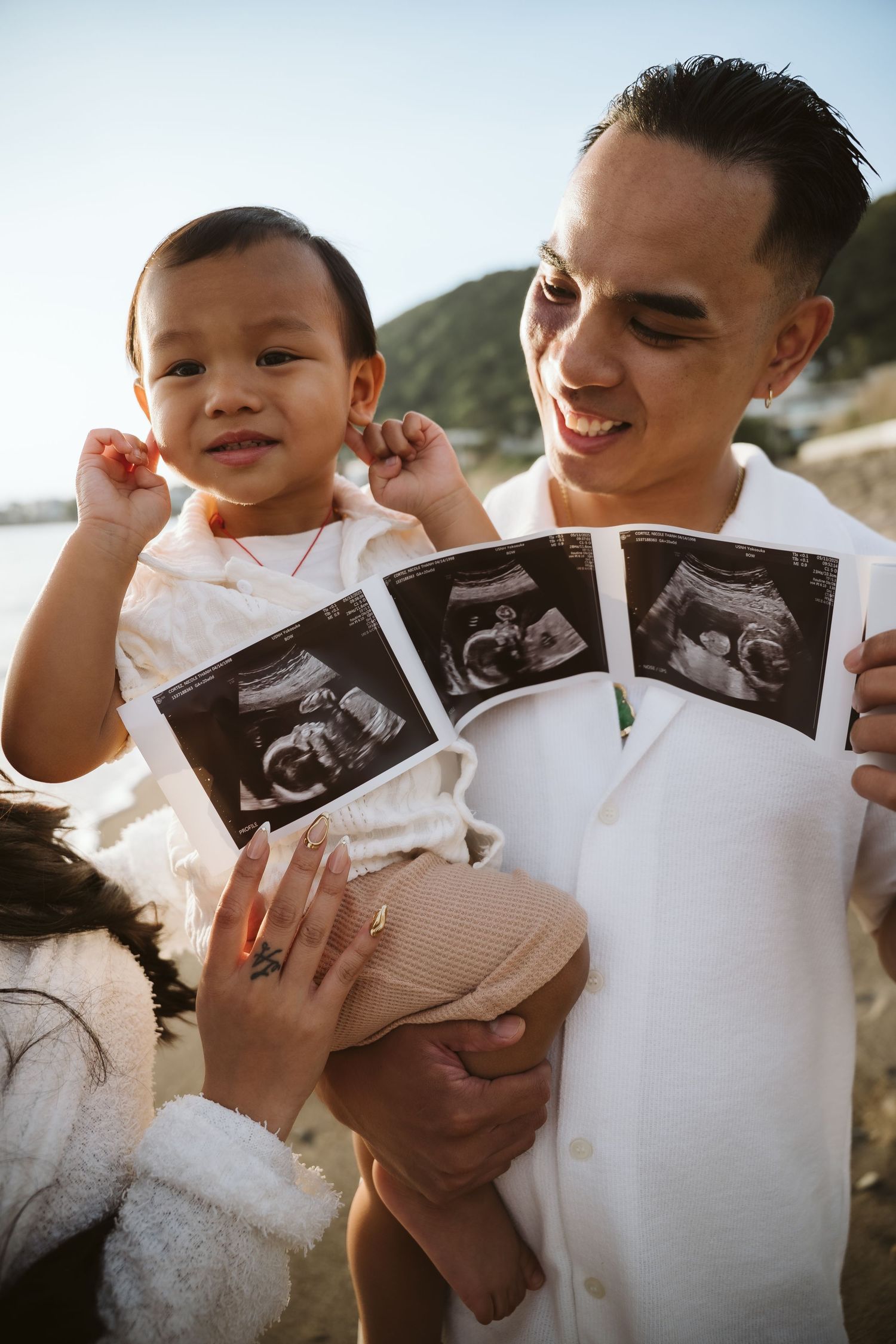 Couple looking at ultrasound photos together at the beach while smiling and embracing.