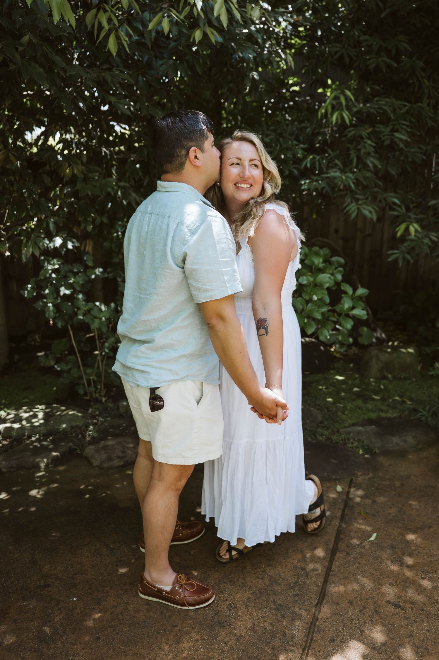 A mother and child share a tender moment together in a garden setting, wearing coordinating white outfits.