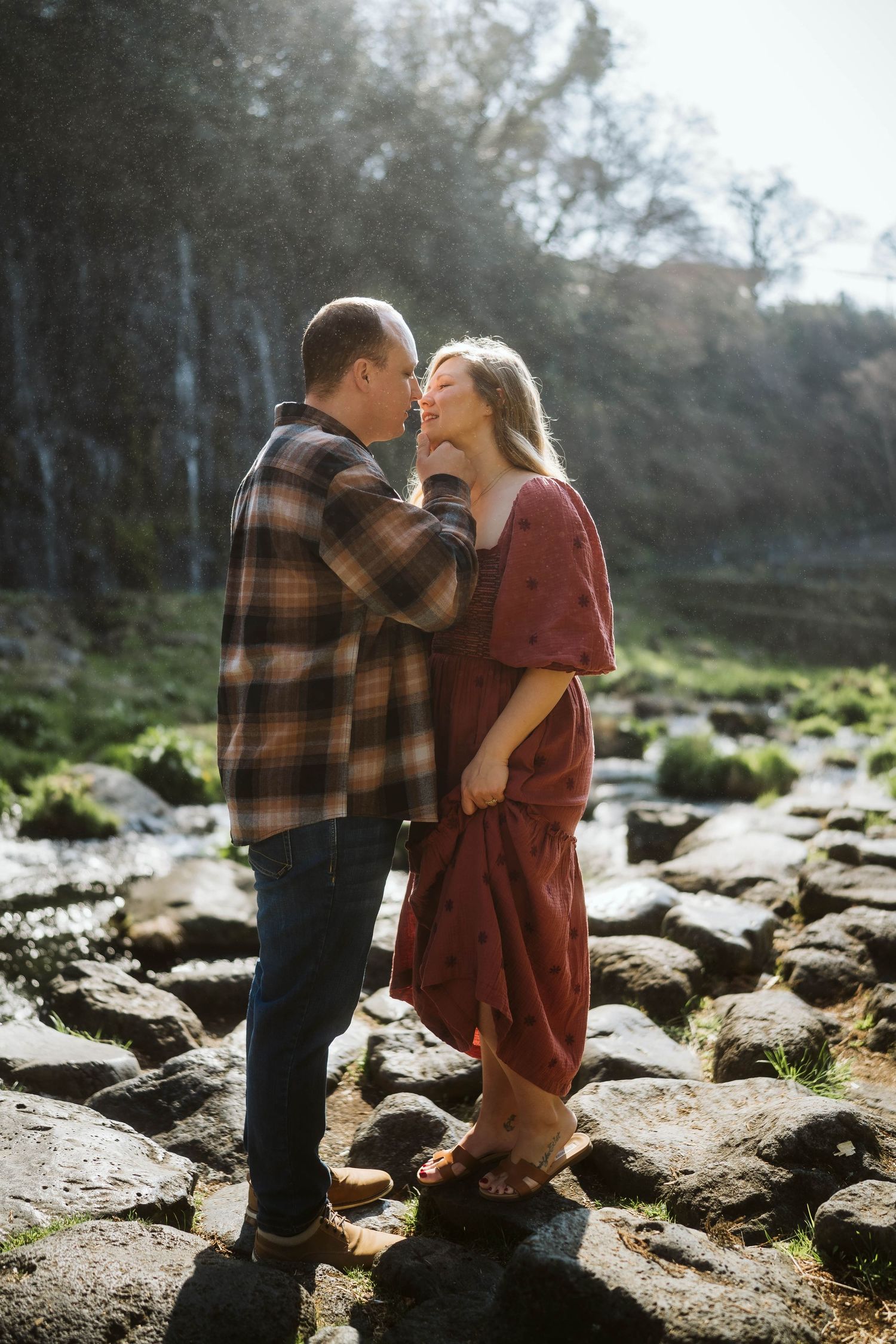 A romantic couple shares tender moments together on rocky terrain during an outdoor photoshoot at dusk.