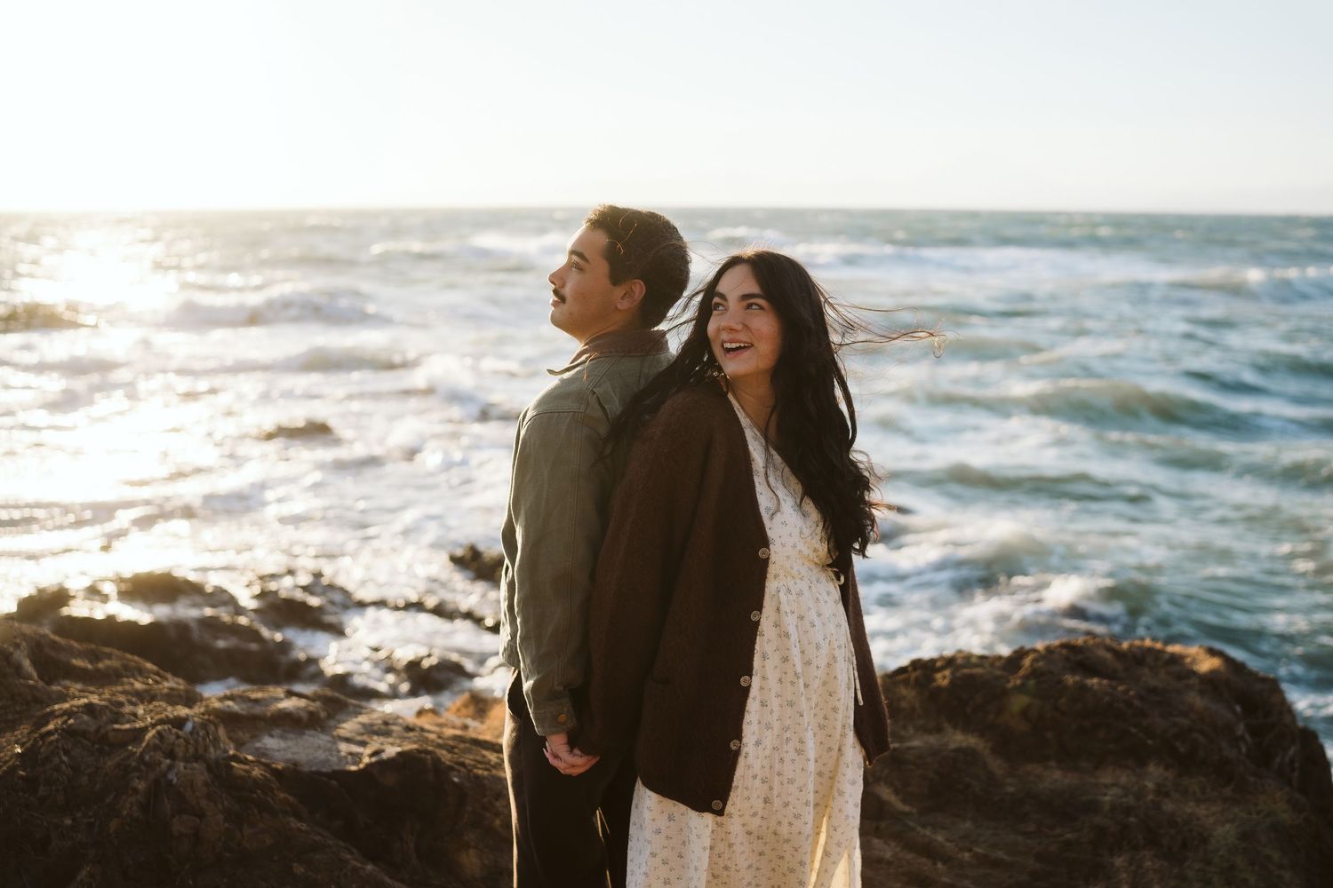 Romantic couple sharing intimate moment on rocky beach during golden hour with ocean waves.