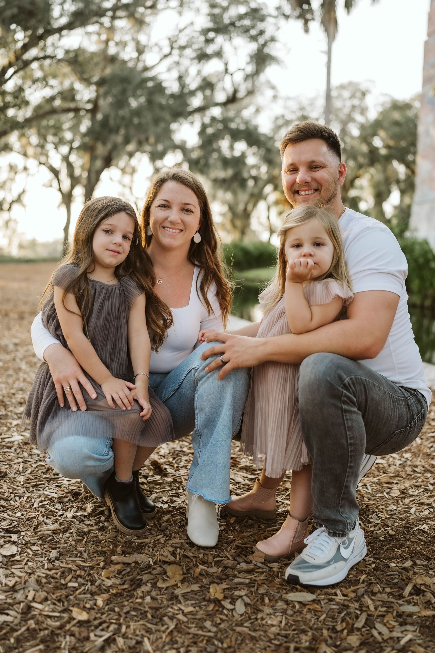 Family poses together on ground covered in fallen leaves during golden hour sunset in an outdoor setting.
