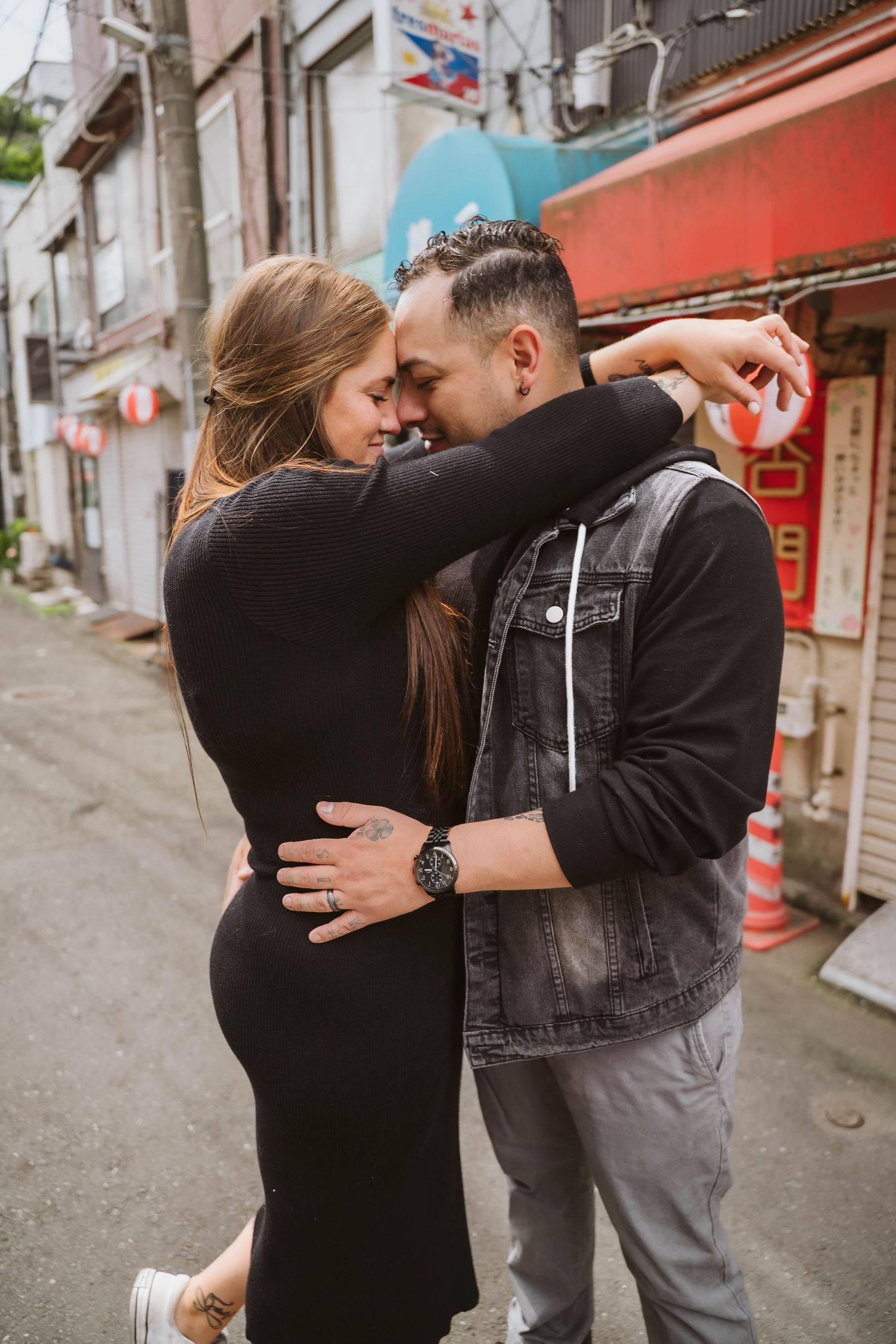 Couple embracing on a narrow urban street with buildings and shops in the background.