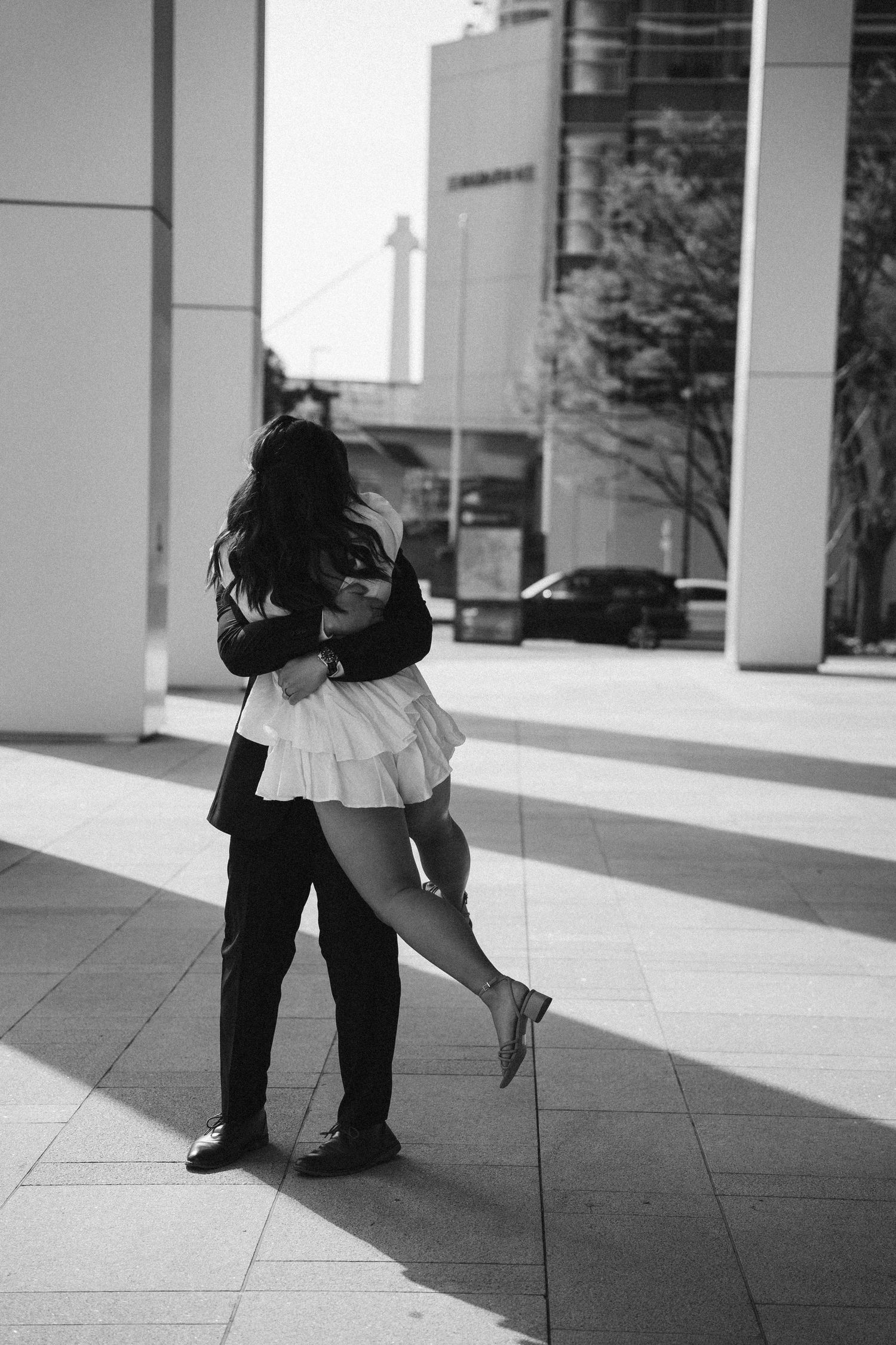A romantic black and white urban photo of a couple embracing with a white pleated skirt visible.