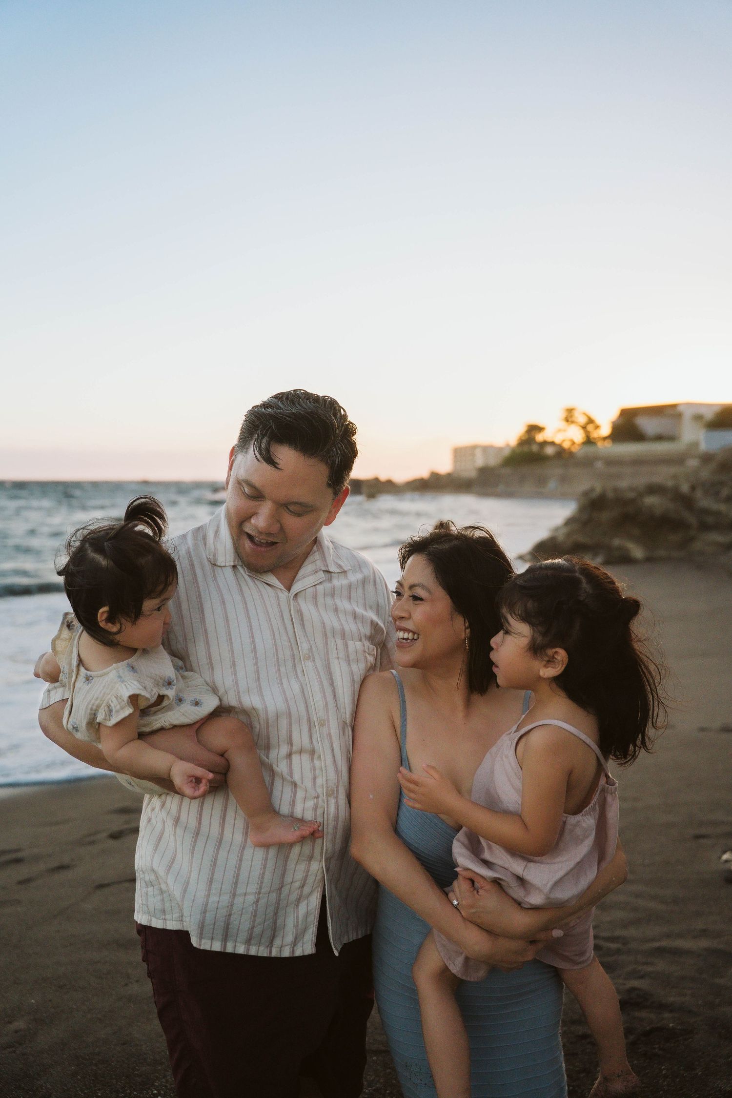 A family shares a joyful moment together on the beach at sunset with coastal homes visible in the background.