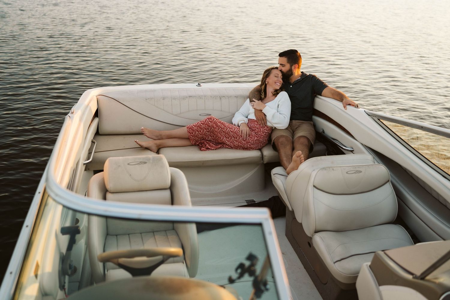 A couple relaxes together on a boat with cream leather seats during sunset on calm waters.