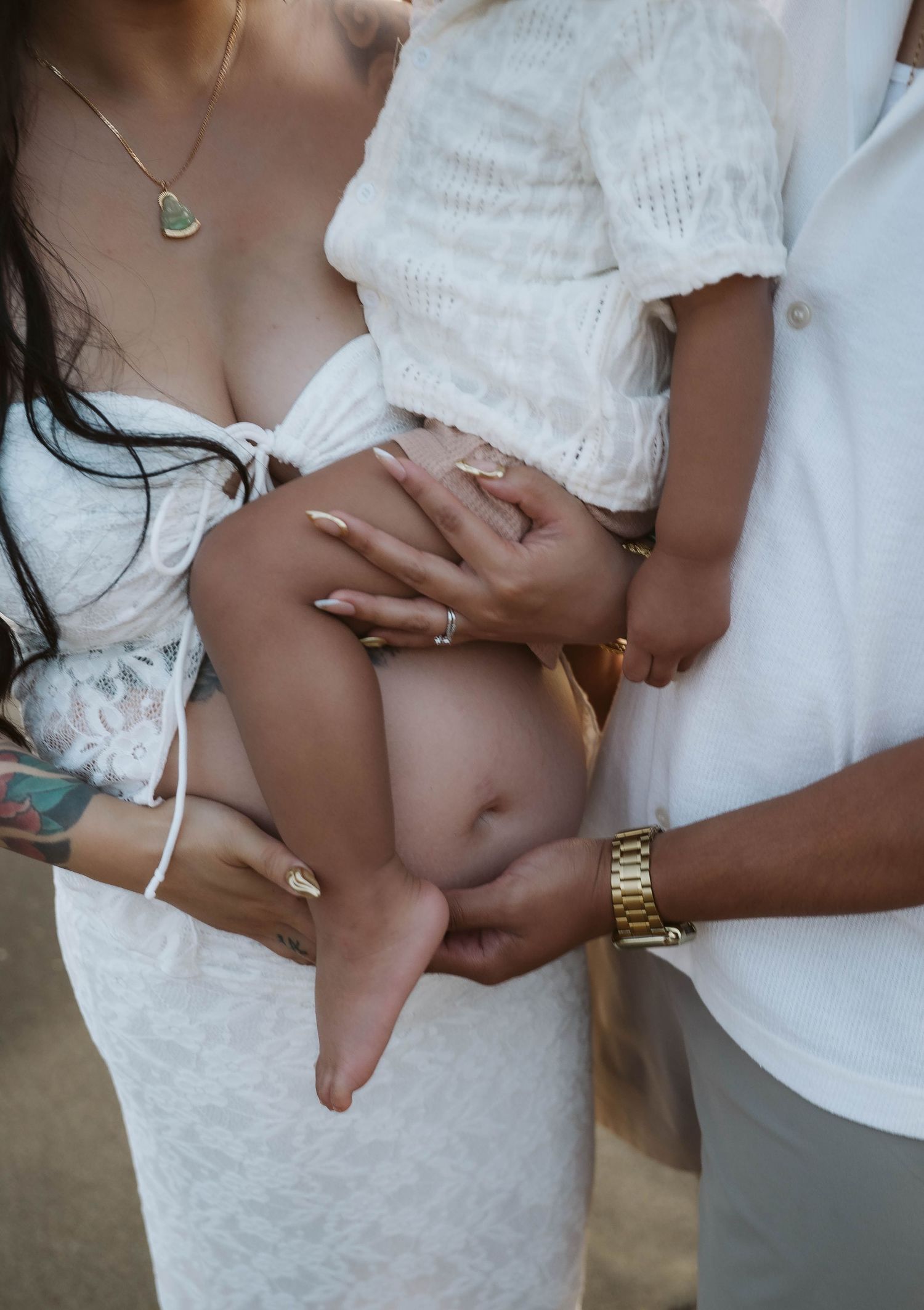 Close up of couple's hands cradling pregnant belly on beach during sunset photoshoot.