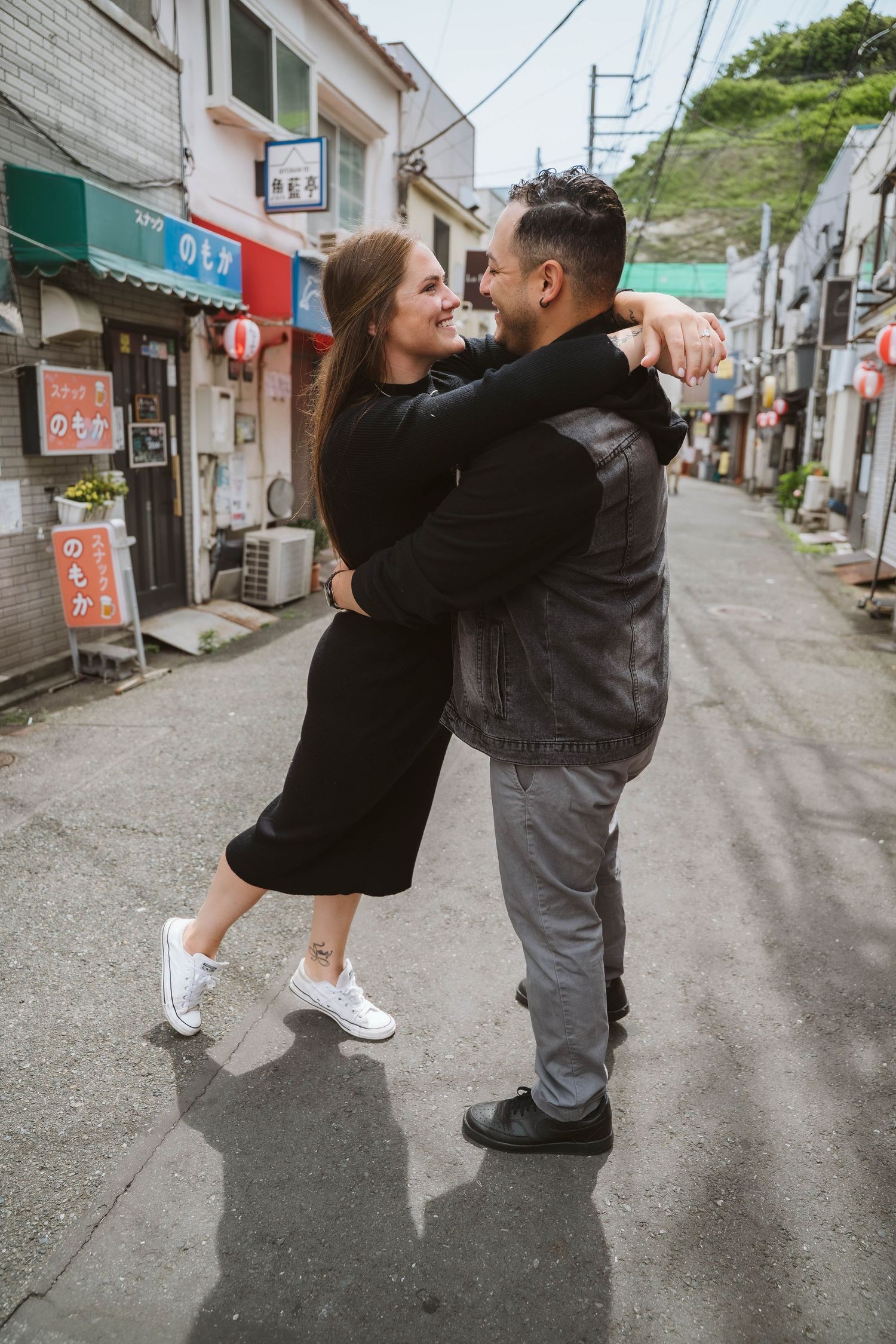 Two people playfully dancing on a quiet street lined with buildings and power lines.