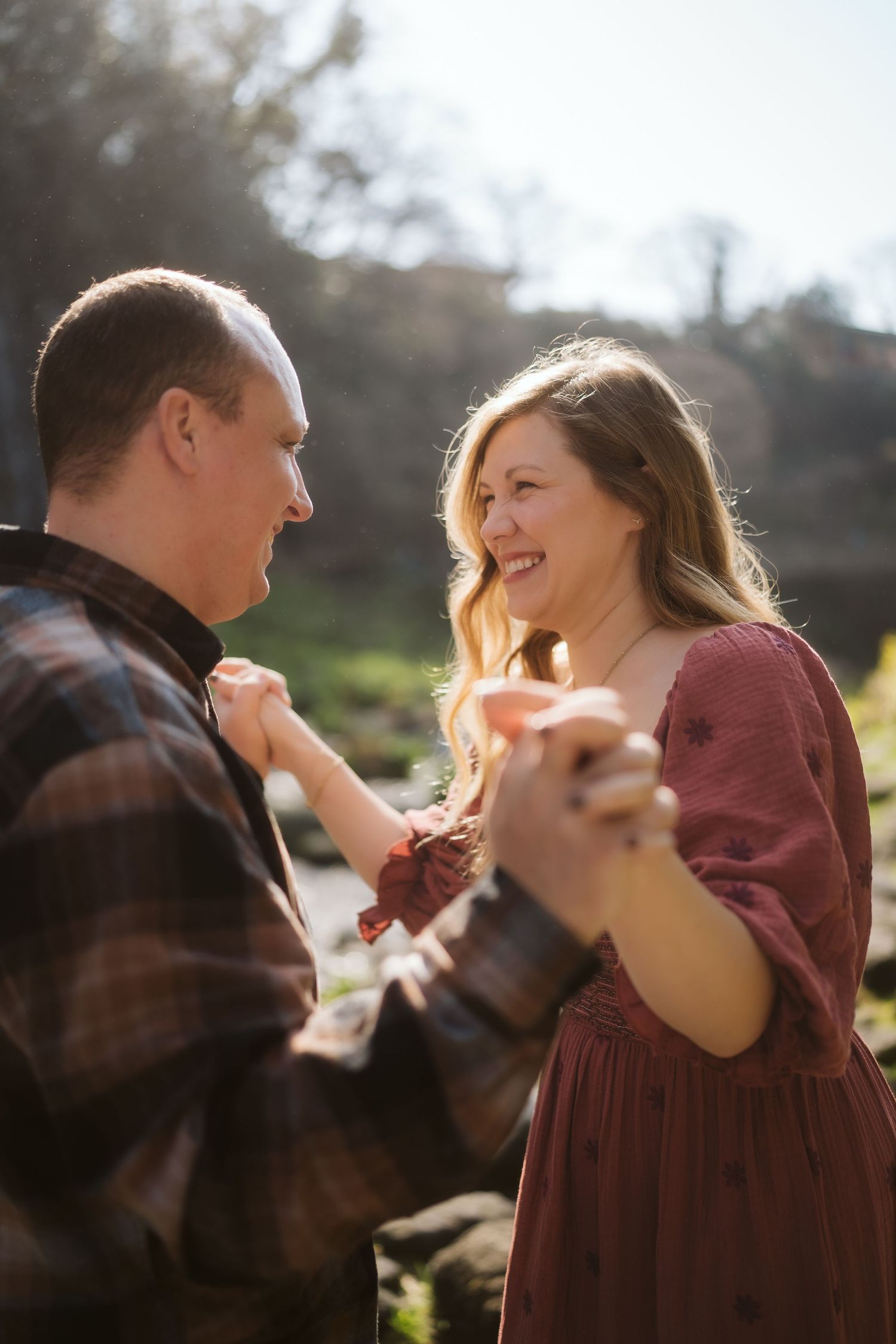 A couple shares a joyful moment together in golden sunlight, laughing and embracing while backlit by warm sunshine.
