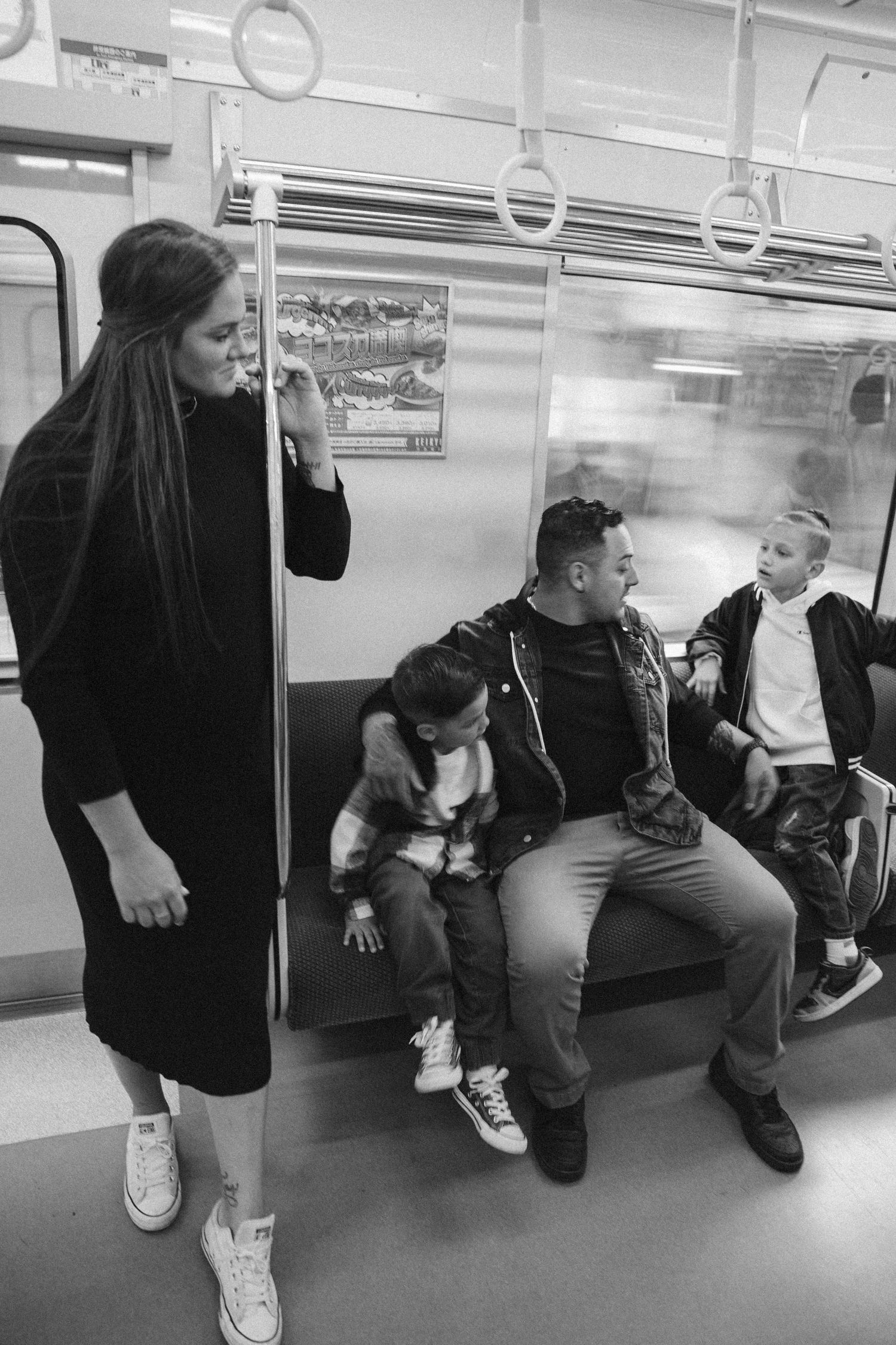A candid black and white moment aboard a subway train showing people sitting and standing together.