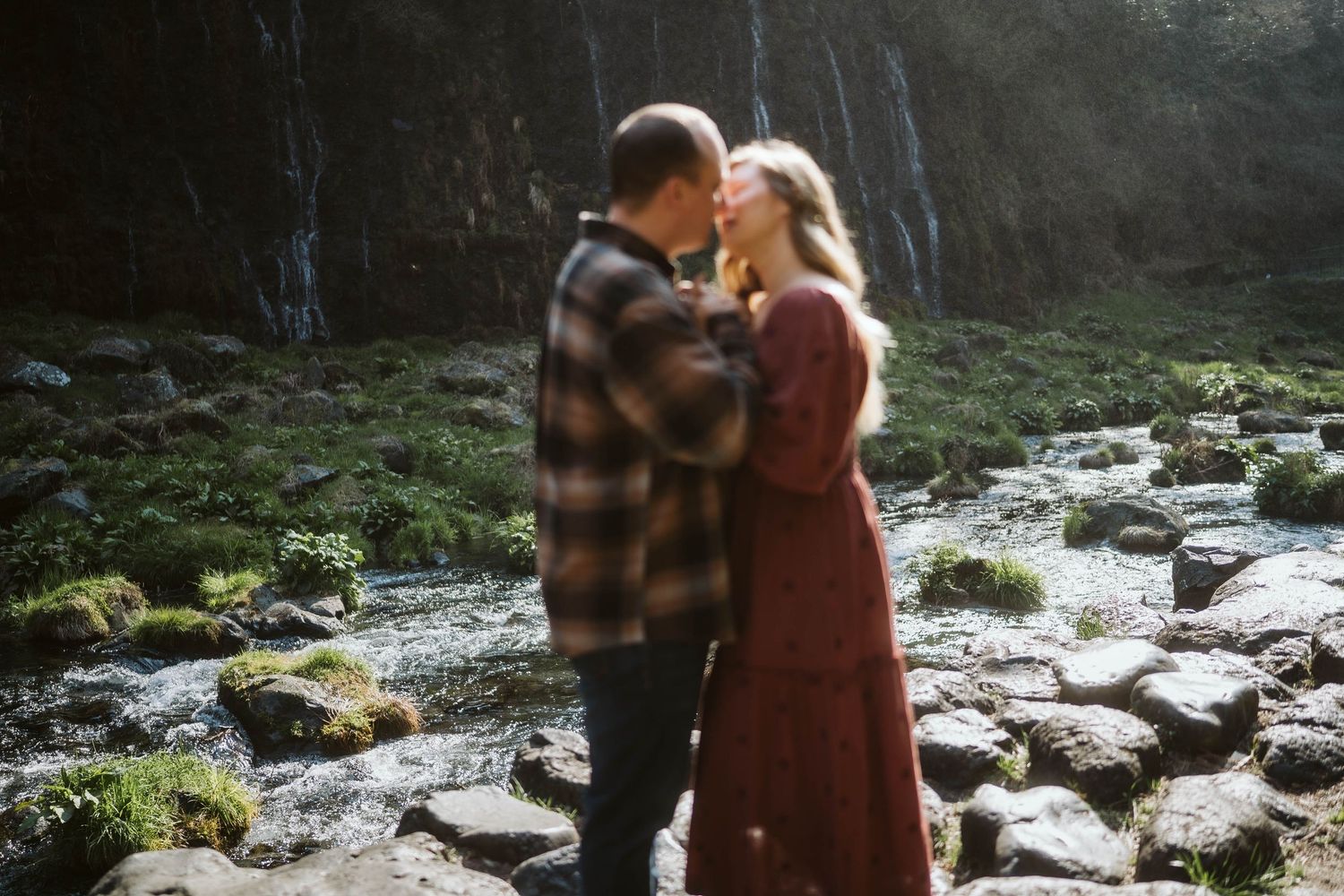 A couple shares a romantic moment together while exploring a scenic rocky stream in a forest setting.