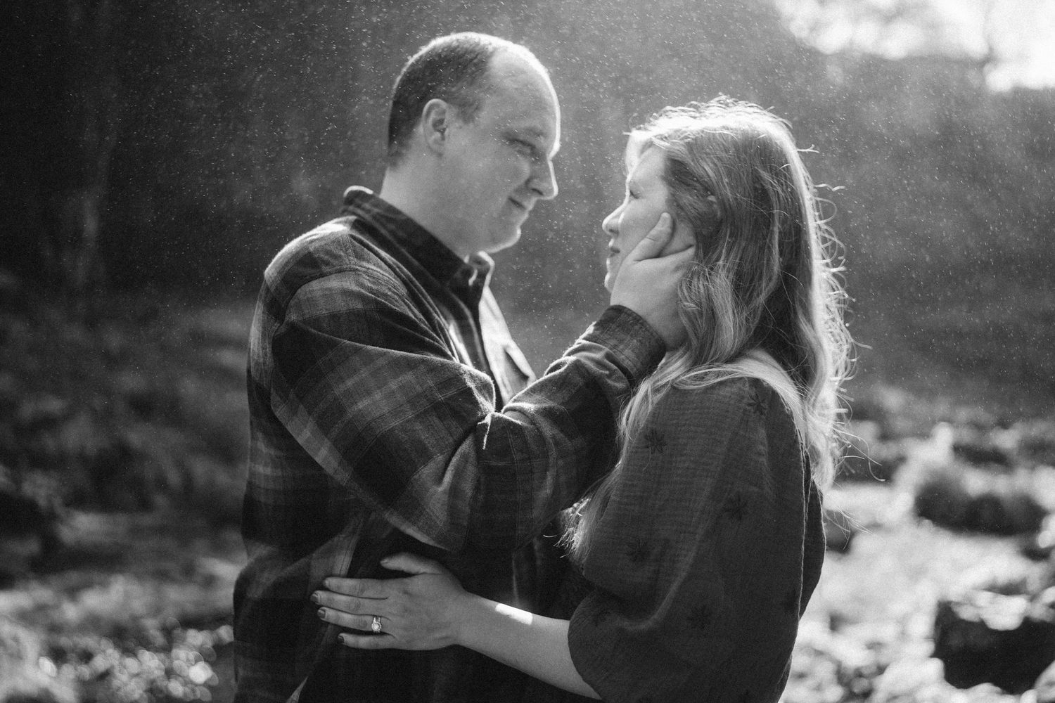 A romantic couple embraces in silhouette against a soft sunlit background in black and white.