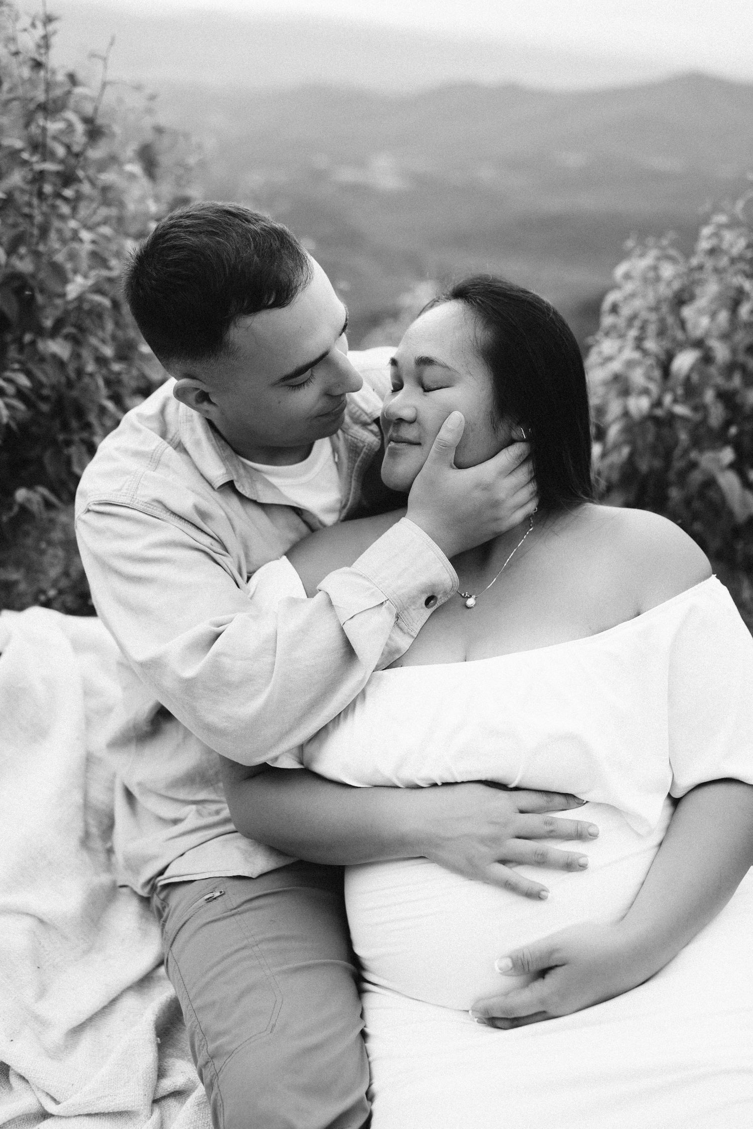 Intimate black and white portrait of a couple sharing a tender moment outdoors with mountains in the background.