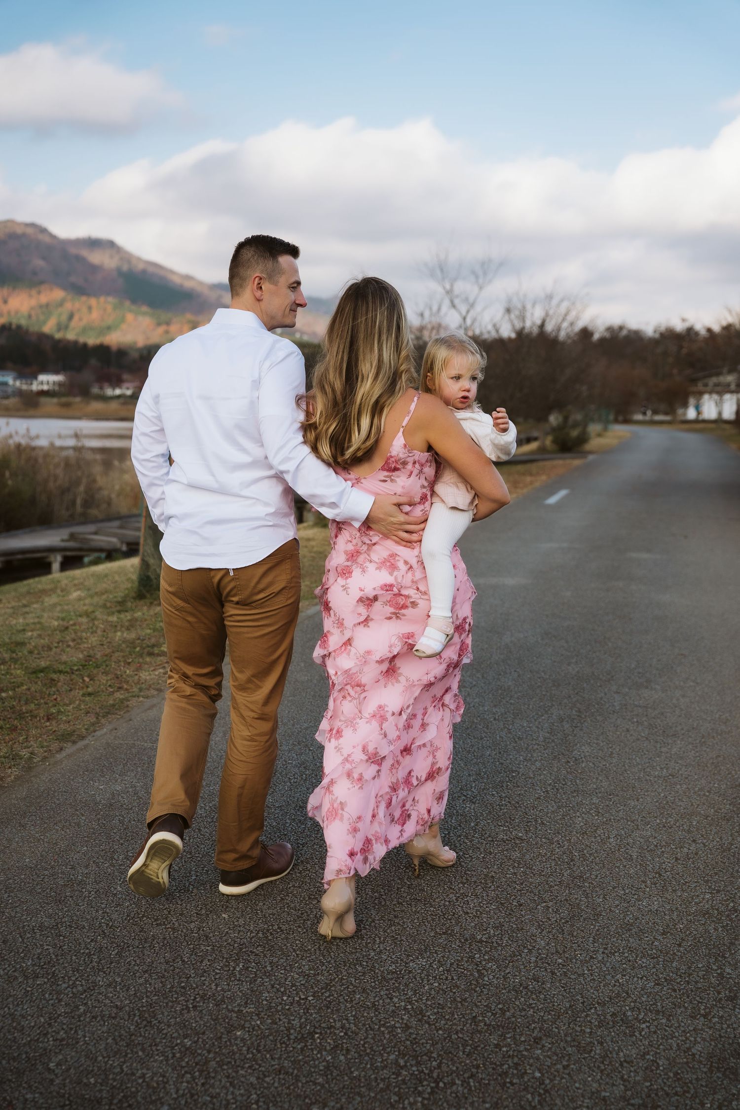 A family walks together on a path with mountains in the background, wearing white and pink floral dress.