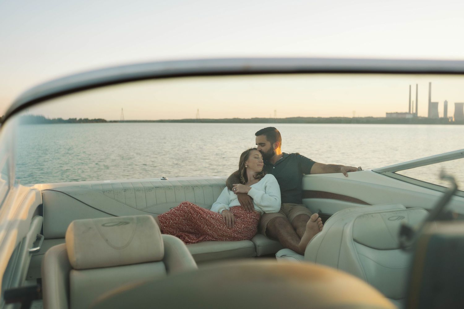 A couple relaxes together on a boat deck with an industrial waterfront visible in the background at sunset.