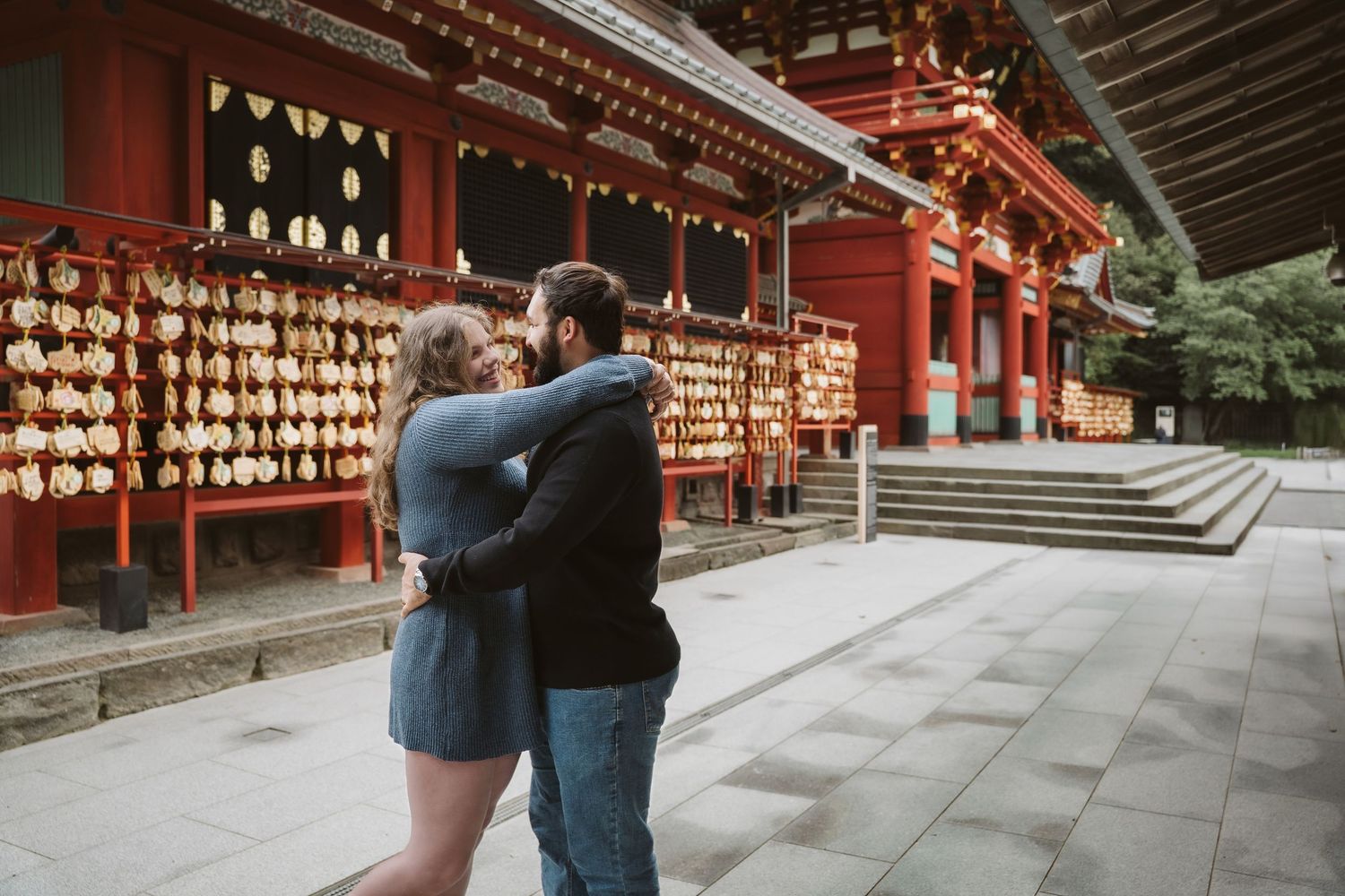 Wooden ema prayer plaques hanging at a traditional Japanese shrine with red architectural details.