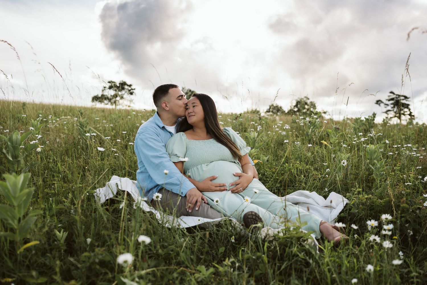 A couple shares a romantic moment while sitting on a blanket in a wildflower meadow during sunset.