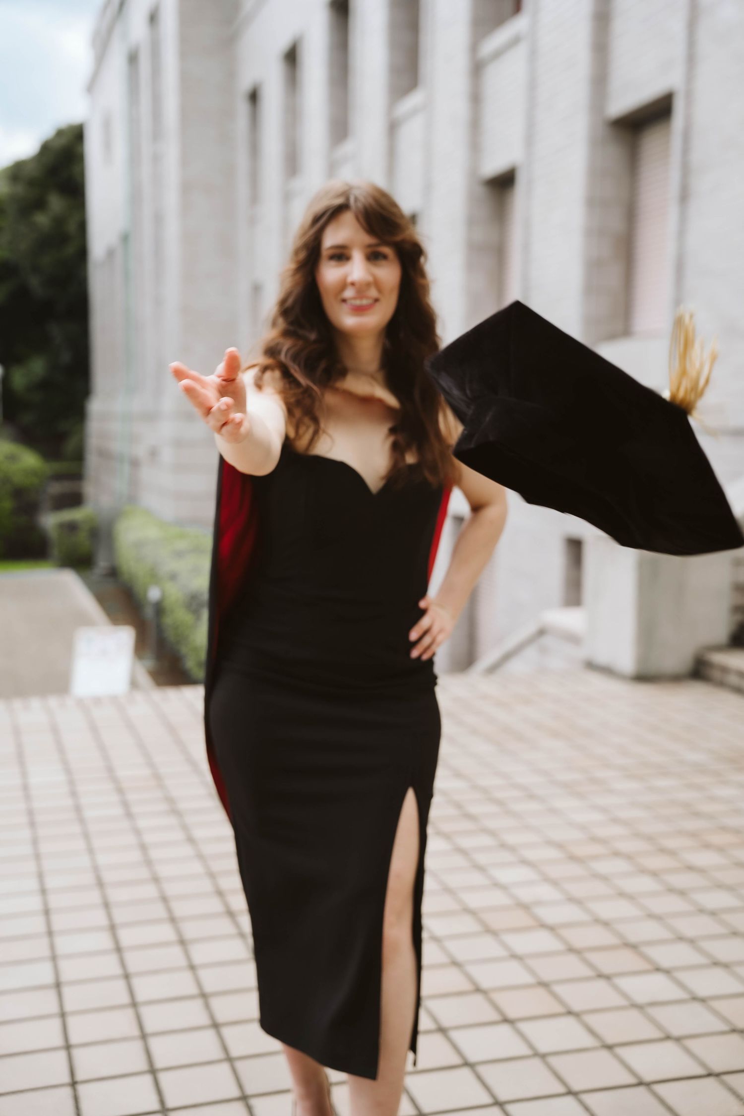 Graduate in black dress celebrating on white stone plaza with joyful movement.